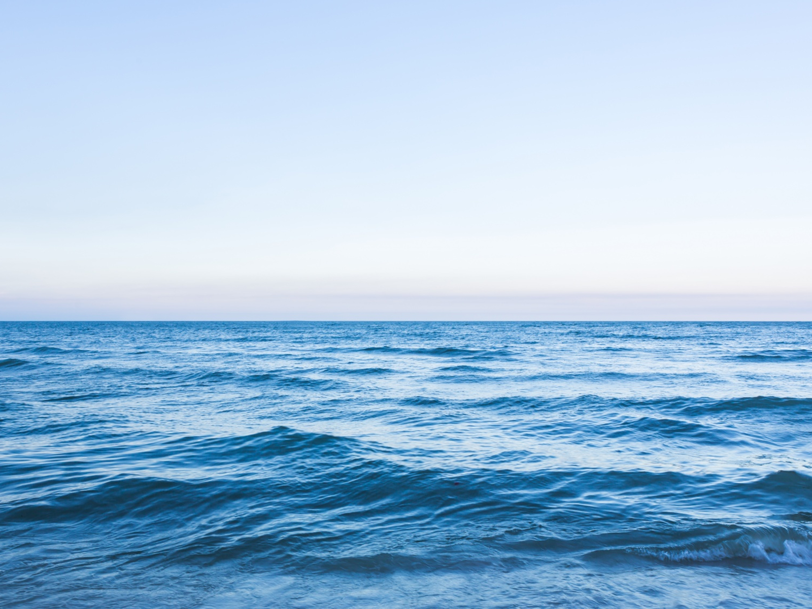 Zdjęcie przedstawia zbiornik wodny z ciemnoniebieską wodą, lekko pofalowaną, nad którą widoczne jest bladoniebieskie niebo.