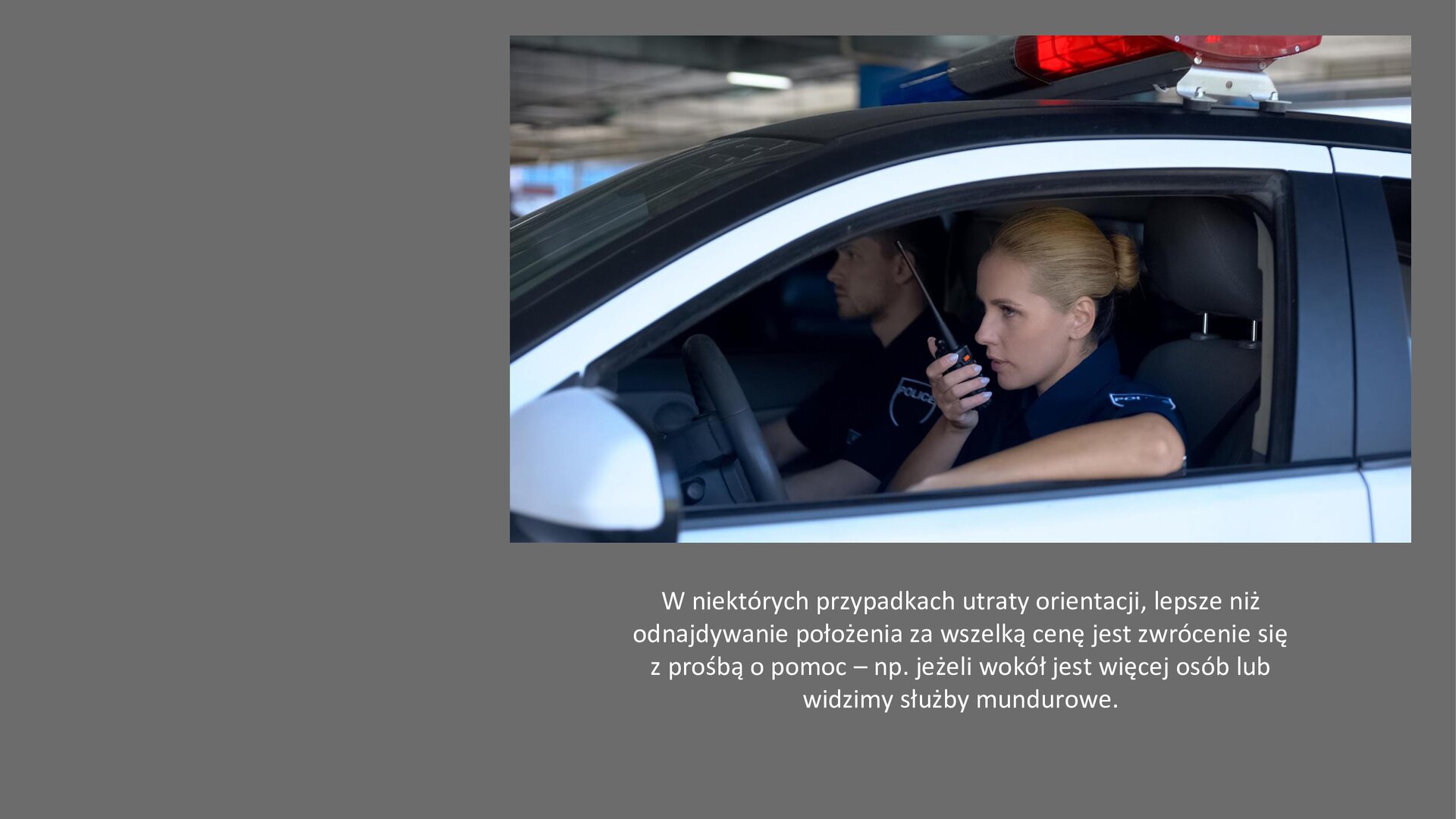 Szary slajd. W prawym górnym rogu zdjęcie przedstawiające samochód policyjny, w środku którego siedzi policjantka i policjant. Kobieta przykłada do ust czarną krótkofalówkę. Pod zdjęciem tekst: „W niektórych przypadkach utraty orientacji, lepsze niż odnajdywanie położenia za wszelką cenę jest zwrócenie się z prośbą o pomoc - na przykład jeżeli wokół jest więcej osób lub widzimy służby mundurowe”.