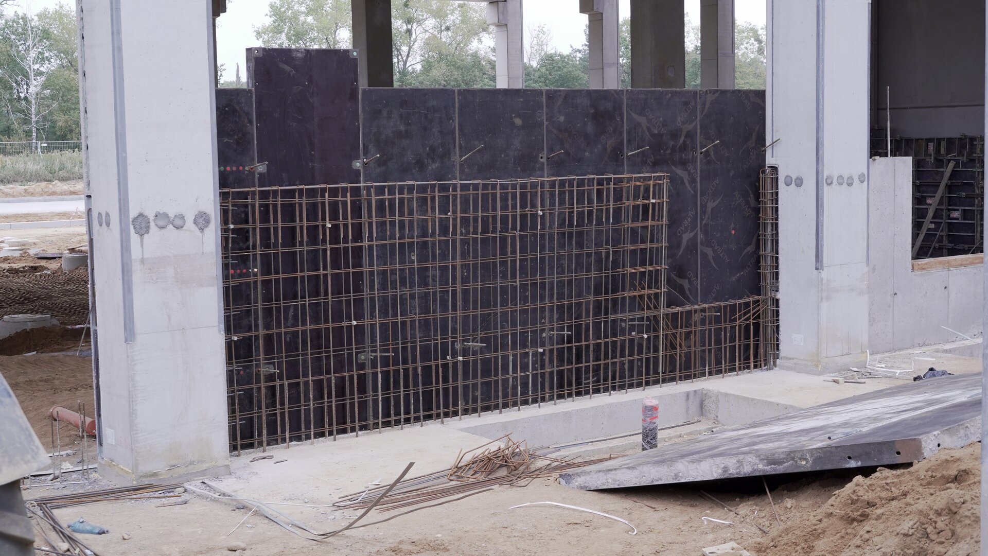 Zdjęcie przedstawia zbrojenie ściany. Pomiędzy obu stronami metalowej konstrukcji złożonej ze stalowych prętów znajdują się dwa białe filary. Za zbrojeniem widać siedem ciemnych płyt.