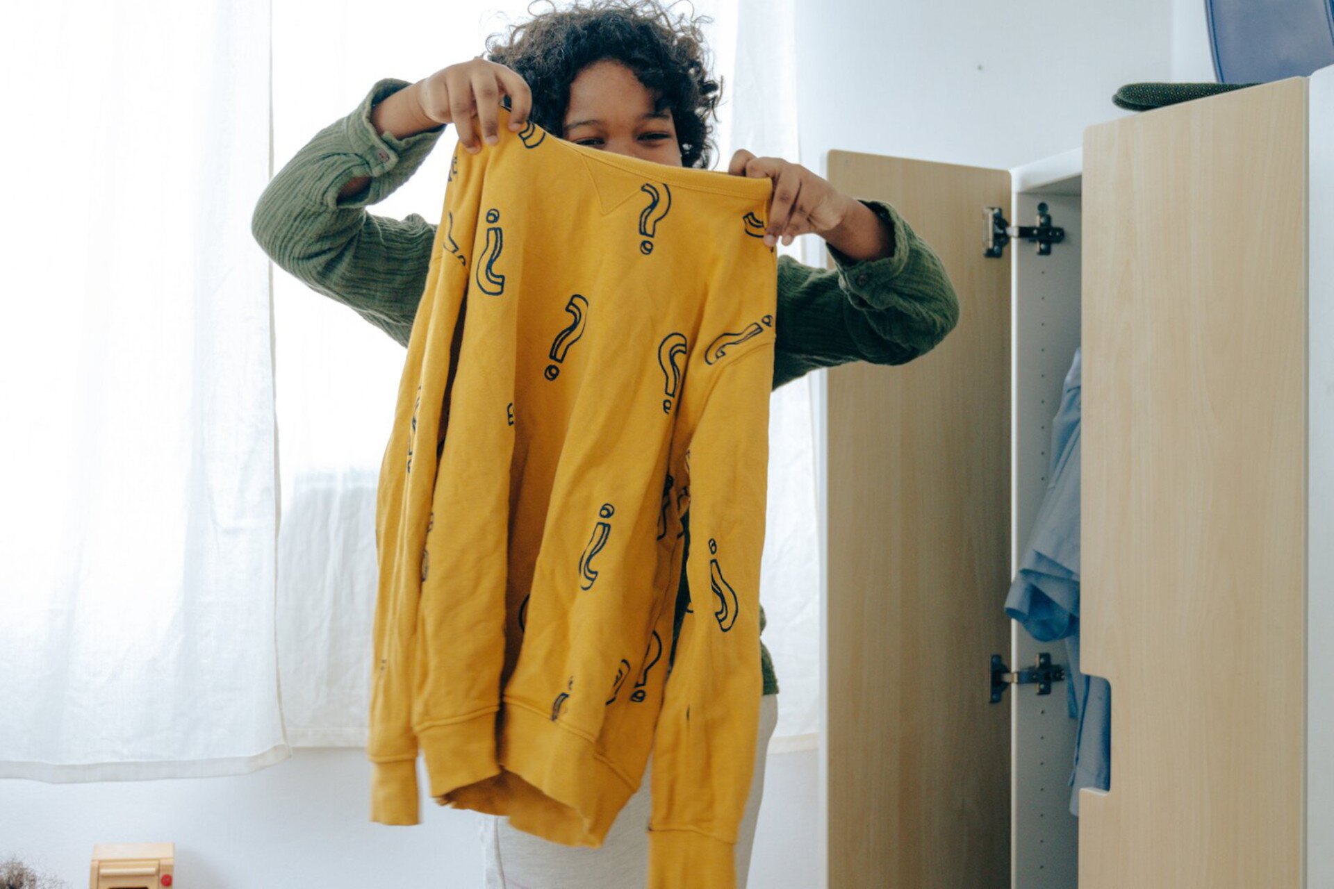 Ilustracja przedstawia chłopca trzymającego żółty sweter w granatowe pytajniki.