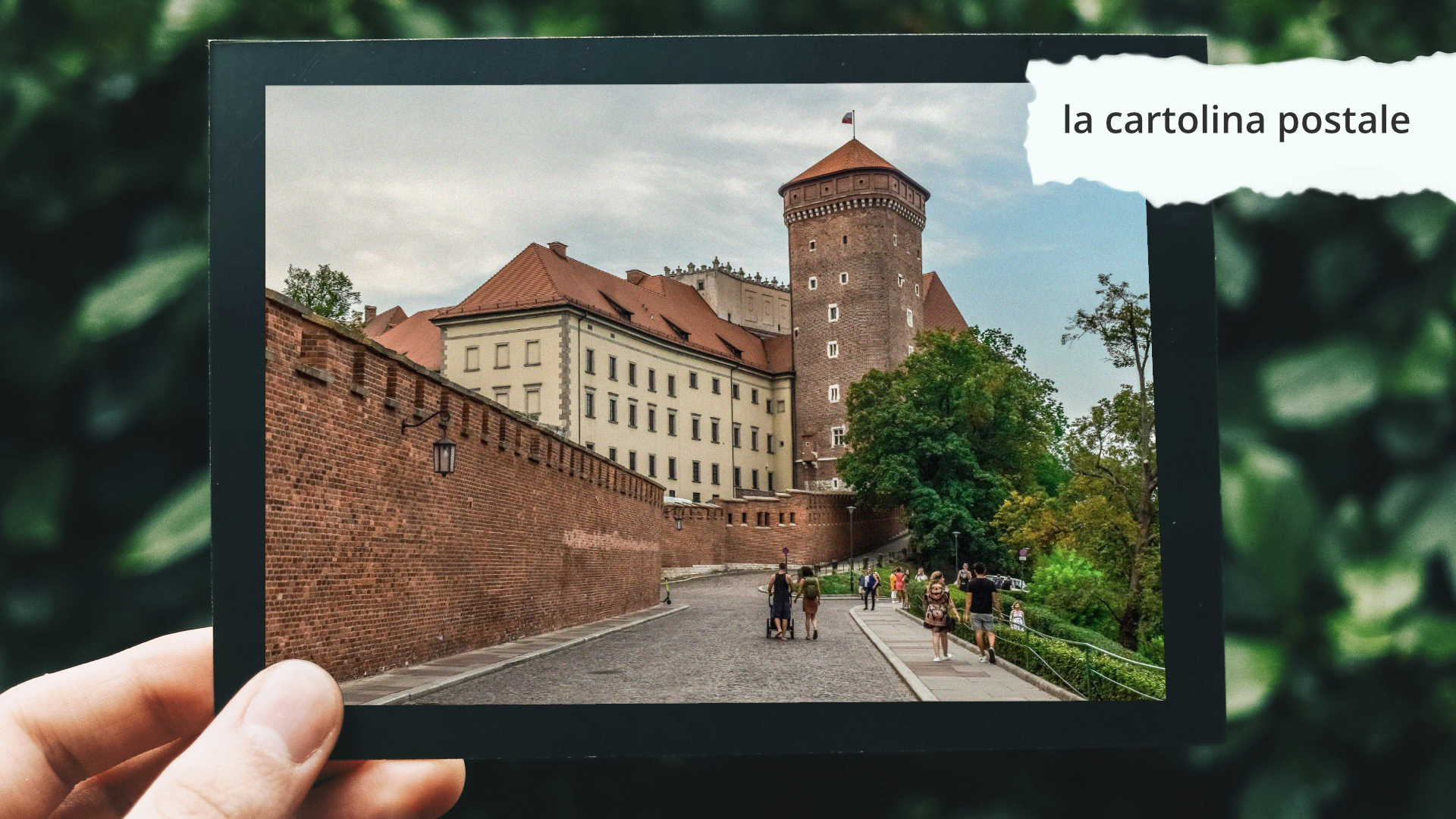 Zdjęcie przedstawia pocztówkę, którą ktoś trzyma w ręku. Na zdjęciu znajduje się napis: la cartolina postale.