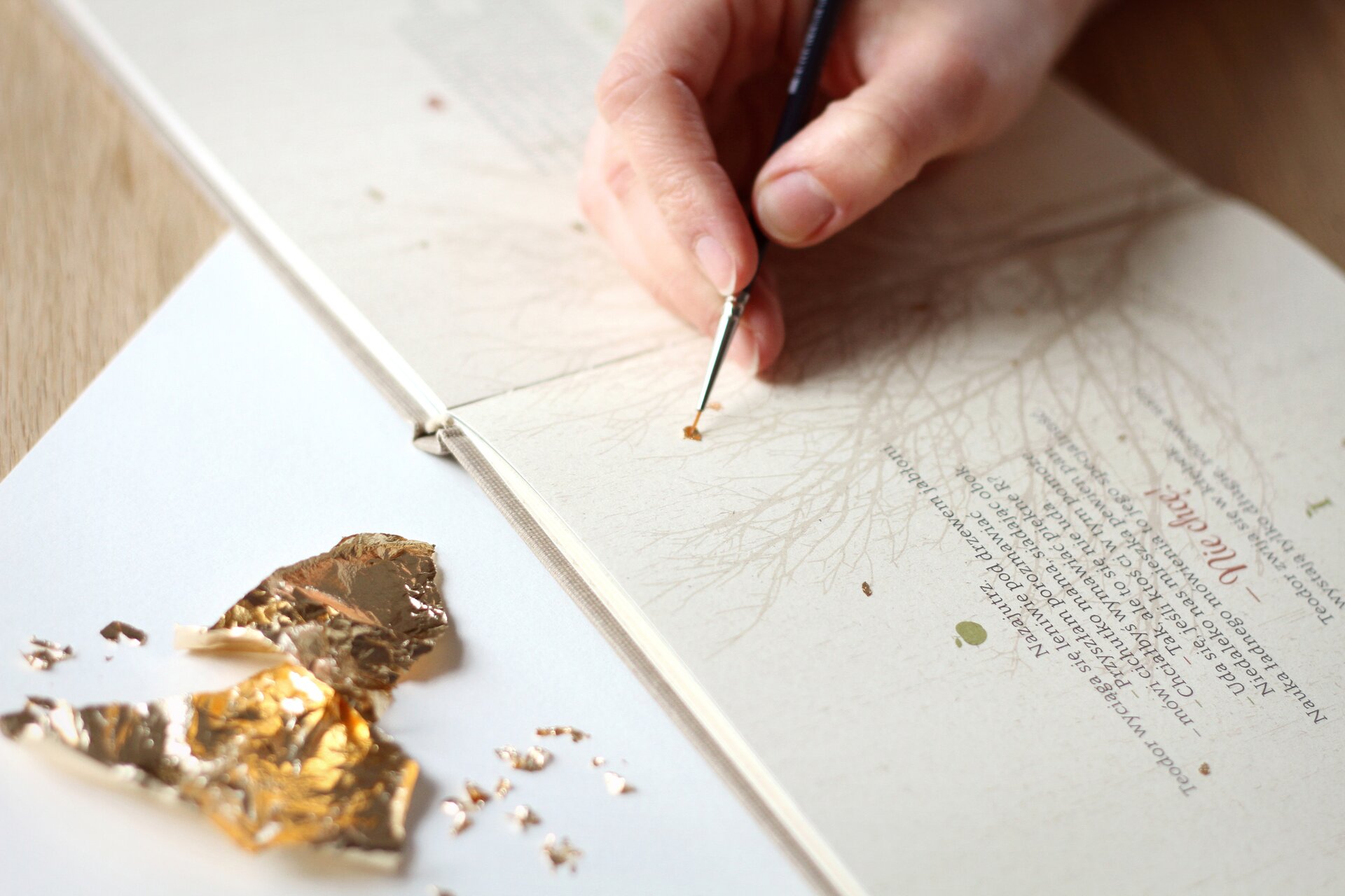 Ilustracja przedstawia fragment tworzenia oprawy graficznej ksiązki dla dzieci Marii Szczodrowskiej: „Teodor”. Widac dłoń, rysującą kropkę na stronie książki.