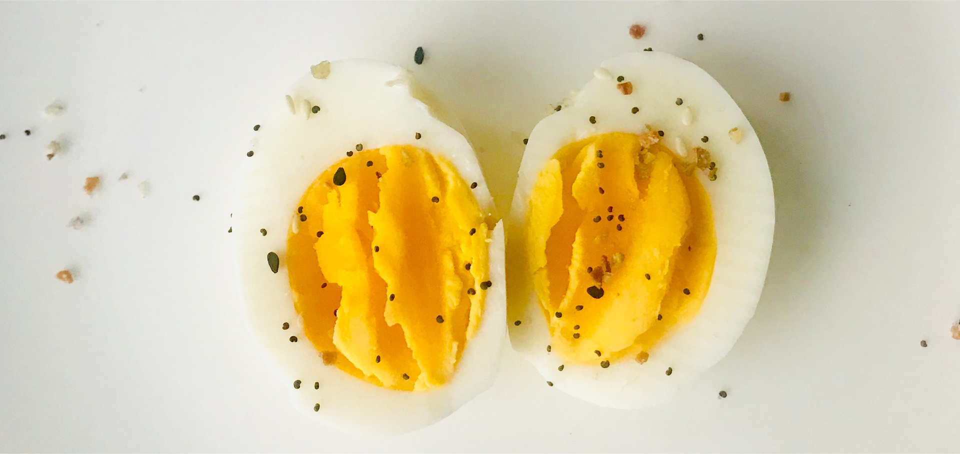Zdjęcie przedstawia ułożone obok siebie dwie połówki jajka ugotowanego na twardo. Jajko jest delikatne posypane solą i pieprzem.
