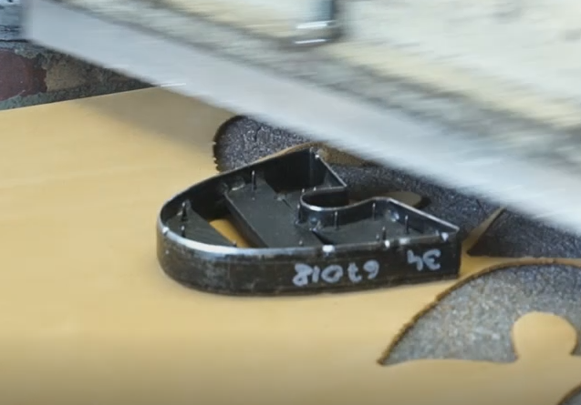 Zdjęcie przedstawia metalowe narzędzie w półokrągłym kształcie, które na brzegu ma zapisaną sygnaturę markerem. Ma niskie brzegi, w środku jest puste. Nagranie tożsame z treścią.