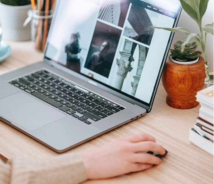 Zdjęcie drugie przedstawia archiwizowanie materiałów. Pokazany jest laptop, który stoi na biurku. W laptopie otwarty jest program do edycji zdjęć. Widoczna jest dłoń, która spoczywa na myszce komputerowej.