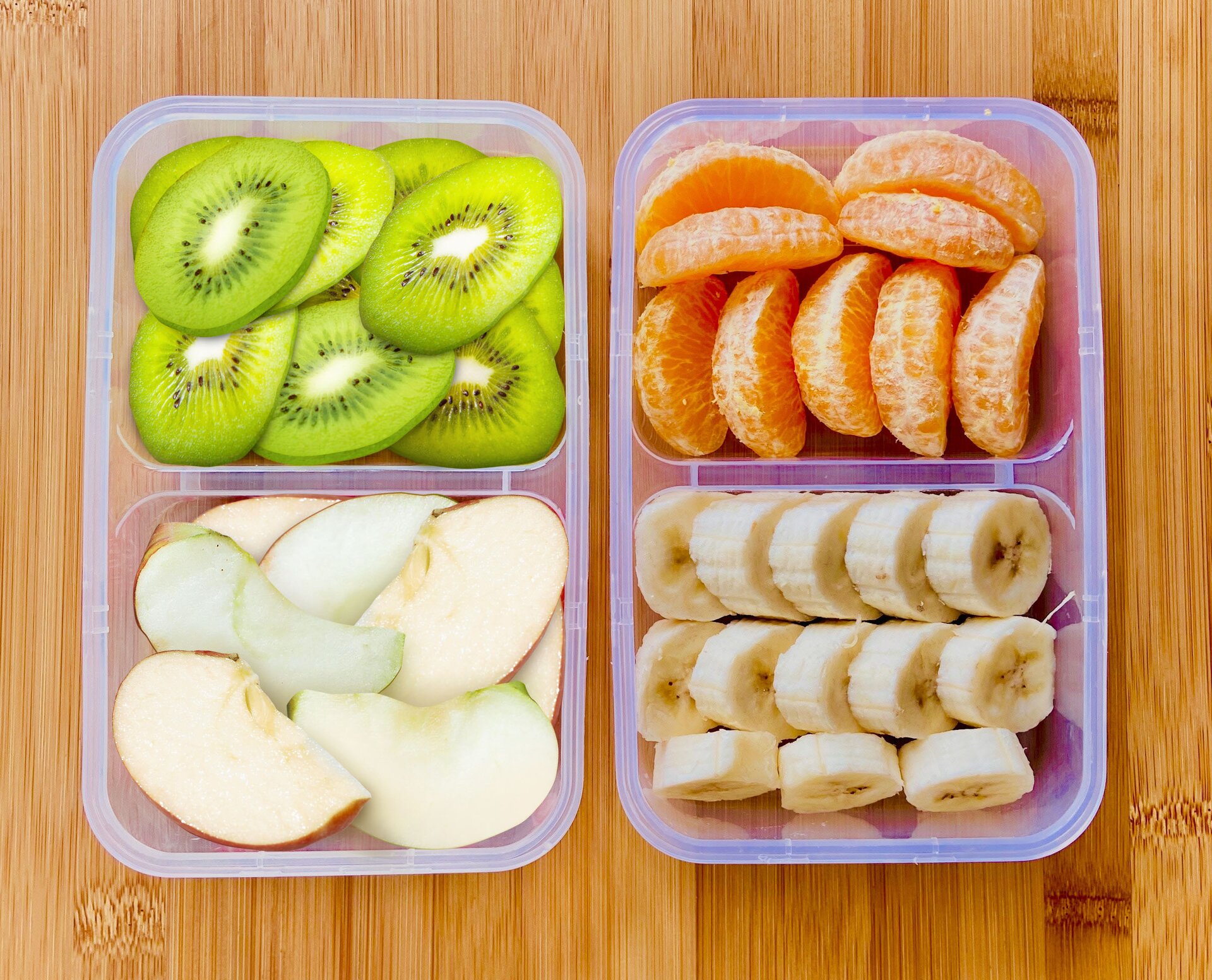 Ilustracja przedstawia pudełka z pokrojonymi kiwi, pomarańczami, jabłkami i bananami.