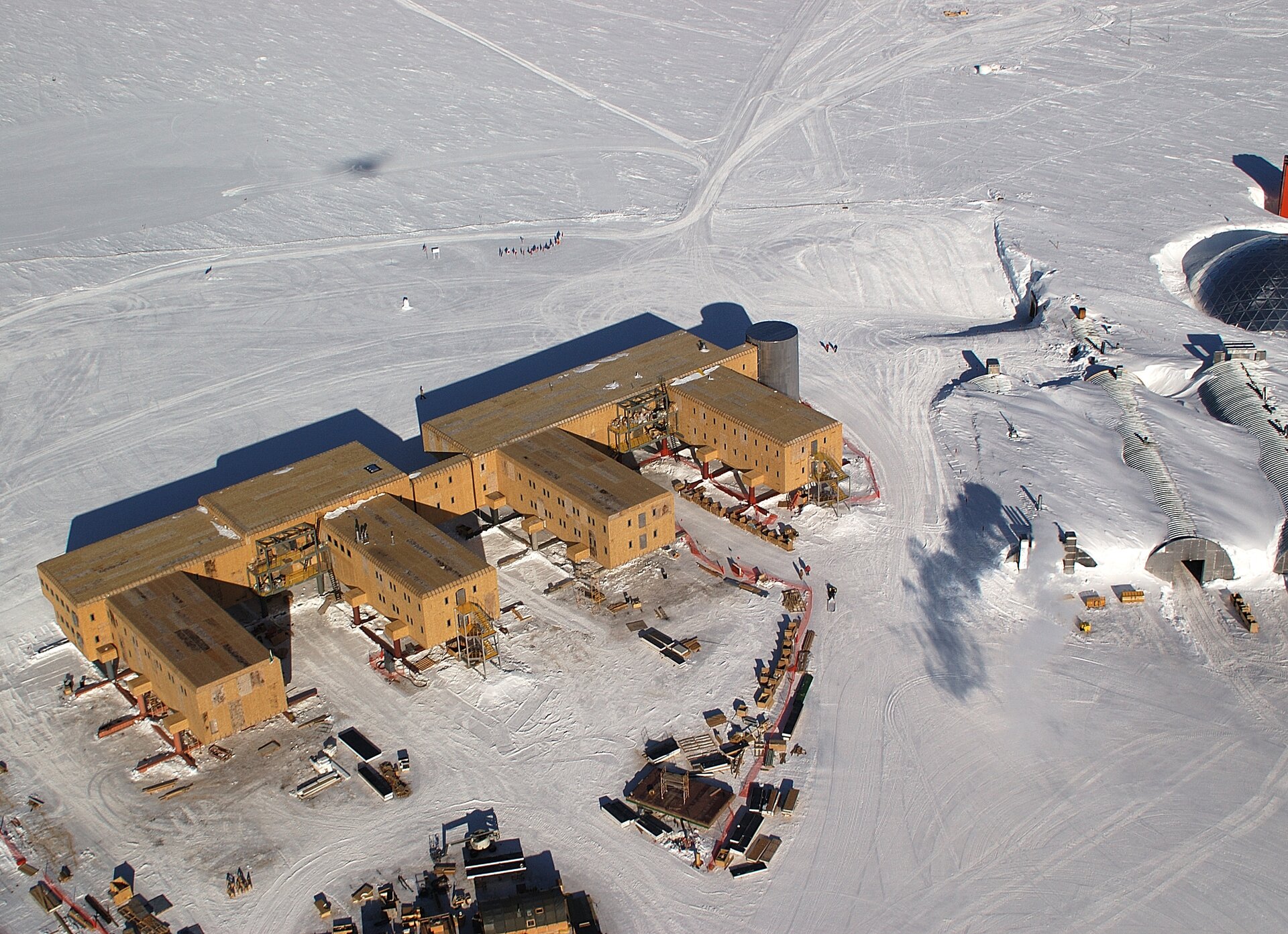 Na zdjęciu lotniczym kompleks kilku jednopiętrowych, jasnobrązowych budynków na ośnieżonym terenie. Z prawej strony trzy zabudowania o kształcie półokrągłych tuneli przysypane śniegiem po dach.