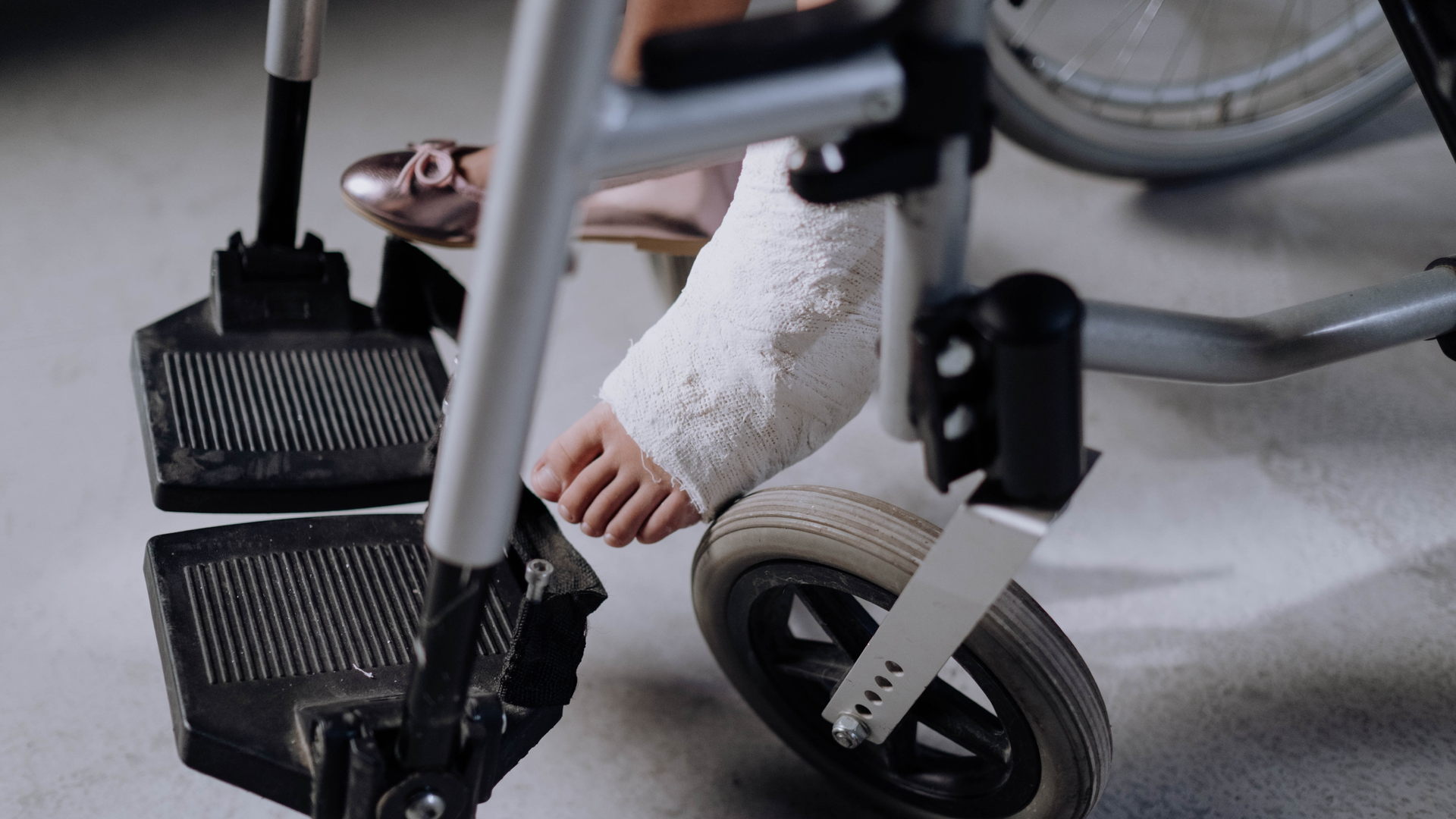 Zdjęcie przedstawia zbliżenie na nogę dziewczyny siedzącej na wózku inwalidzkim. Dziewczyna ma lewą stopę w gipsie.