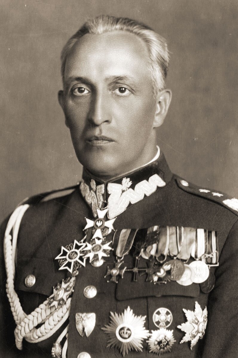 Na zdjęciu mężczyzna o podłużnej twarzy, małych ustach oraz krótkich włosach zaczesanych do tyłu. Ubrany jest w mundur wojskowy, na którym jest wiele medali i orderów.