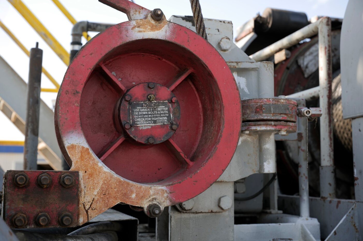 Zdjęcie przedstawia kotwicę martwego końca liny czyli element, do którego zamontowany jest koniec liny wiertniczej, wyposażony w czujnik siły do określania wskazań ciężarowskazu. Do czerwonego elementu w kształcie walca tak zwanej kotwicy martwego końca liny przymocowany jest martwy koniec liny wiertniczej. Lina wiertnicza wykonana jest ze stali z nachodzących na siebie splotek. W połowie wysokości czerwonego walca umieszczony jest do niego prostopadle (w poziomie) drugi mniejszy czerwony walec, który stanowi czujnik siły do określania wskazanego ciężarowskazu.