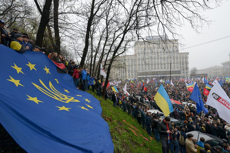 Zdjęcie przedstawia tłum manifestujących ludzi. Trzymają flagi Ukrainy oraz Unii Europejskiej. Po lewej stronie na wzniesieniu grupa osób trzyma dużą flagę Unii Europejskiej z dodanym złotym trójzębem z herbu Ukrainy.