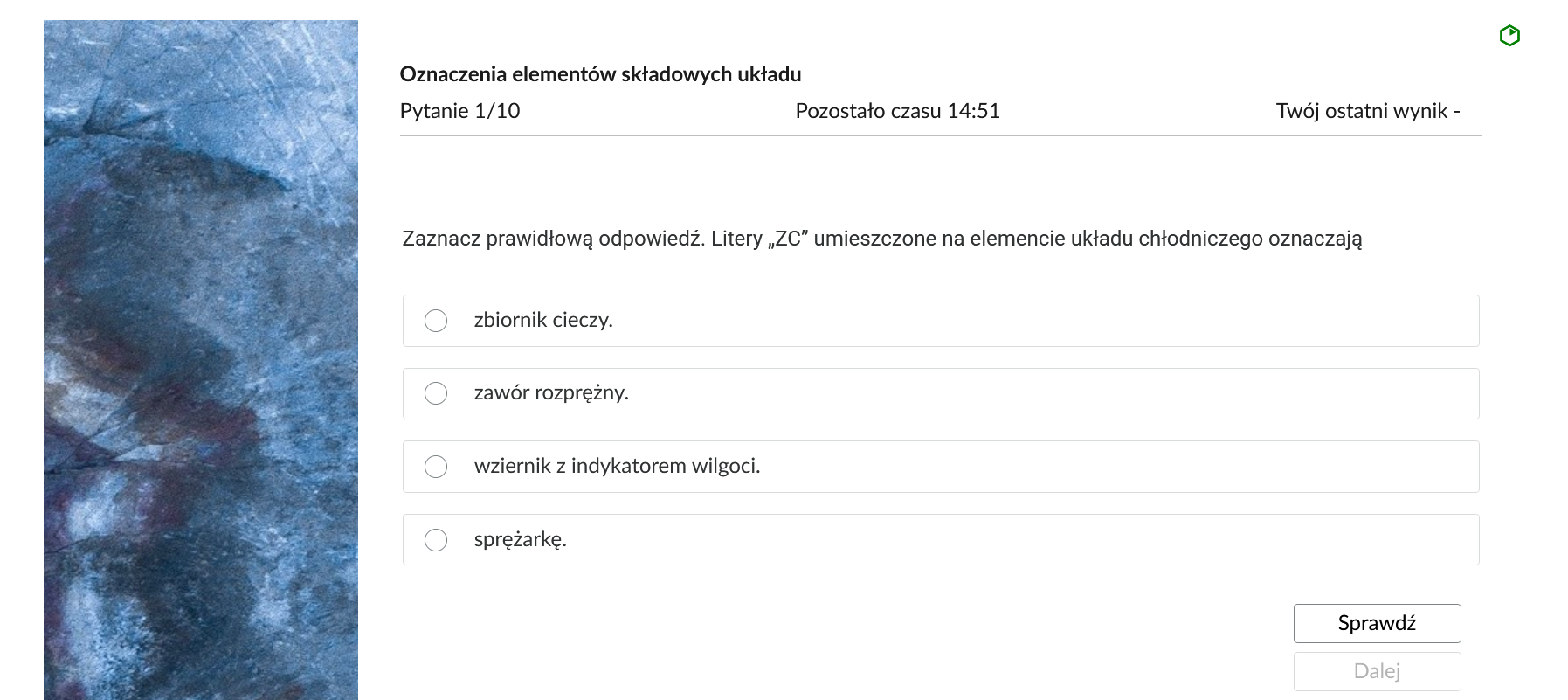 Grafika przedstawia przykładowe zadanie testowe. Ponad poleceniem widać numer pytania, czas, który pozostał na wypełnianie testu, oraz ostatni uzyskany wynik. Pod poleceniem znajdują się możliwe odpowiedzi. W prawym dolnym rogu panelu z zadaniem znajdują się dwa przyciski. Są to "Sprawdź" oraz "Dalej".