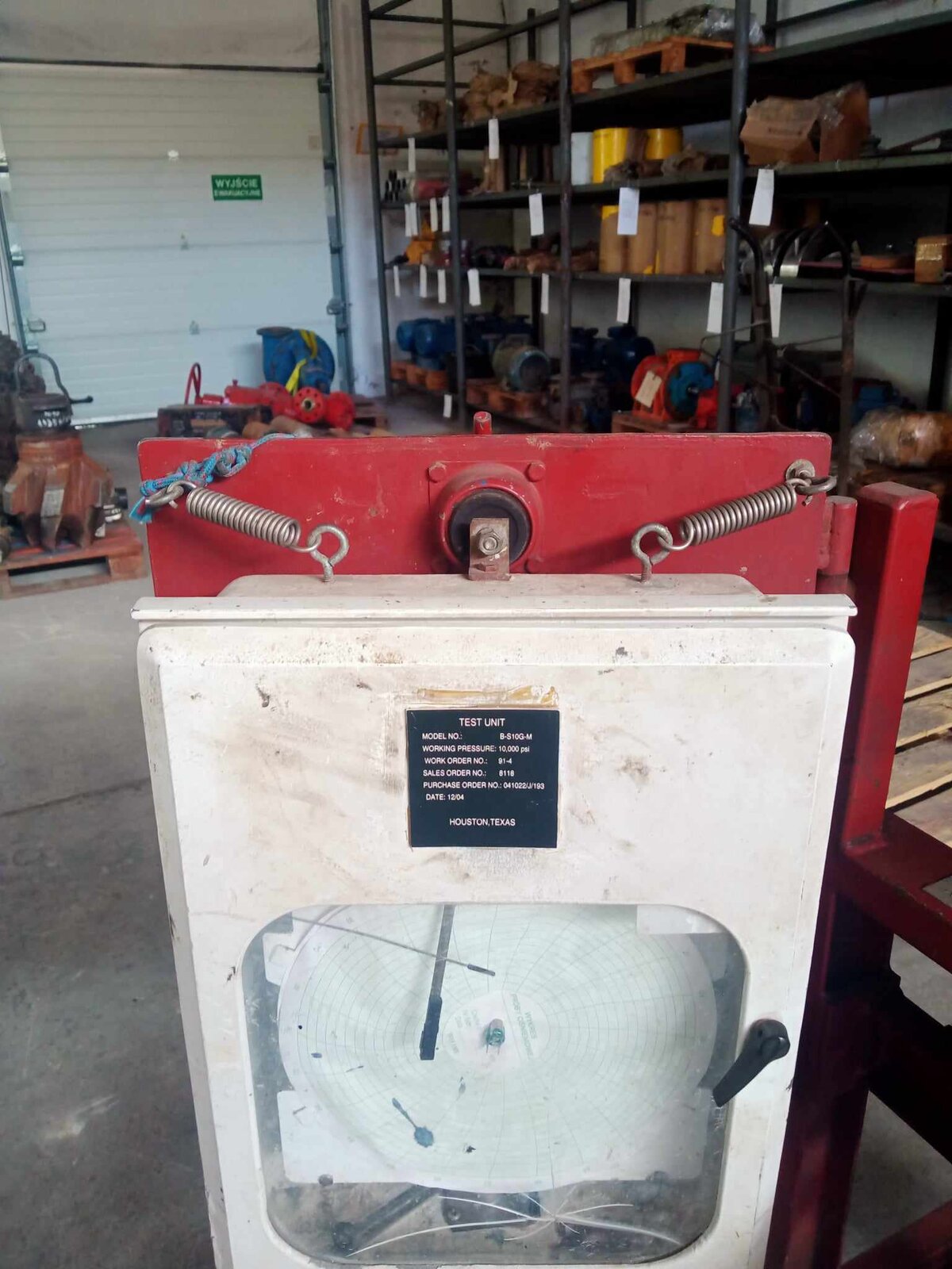 Na zdjęciu widoczny jest rekordograf. Rekordograf to specjalne urządzenie służące do analizowania i zbierania danych. Składa się on z skrzynki z wizjerem. W środku znajduje się okrągła tarcza, na której zapisywane są dane. Nad wizjerem znajduje się tabliczka z parametrami jednostki testowej.