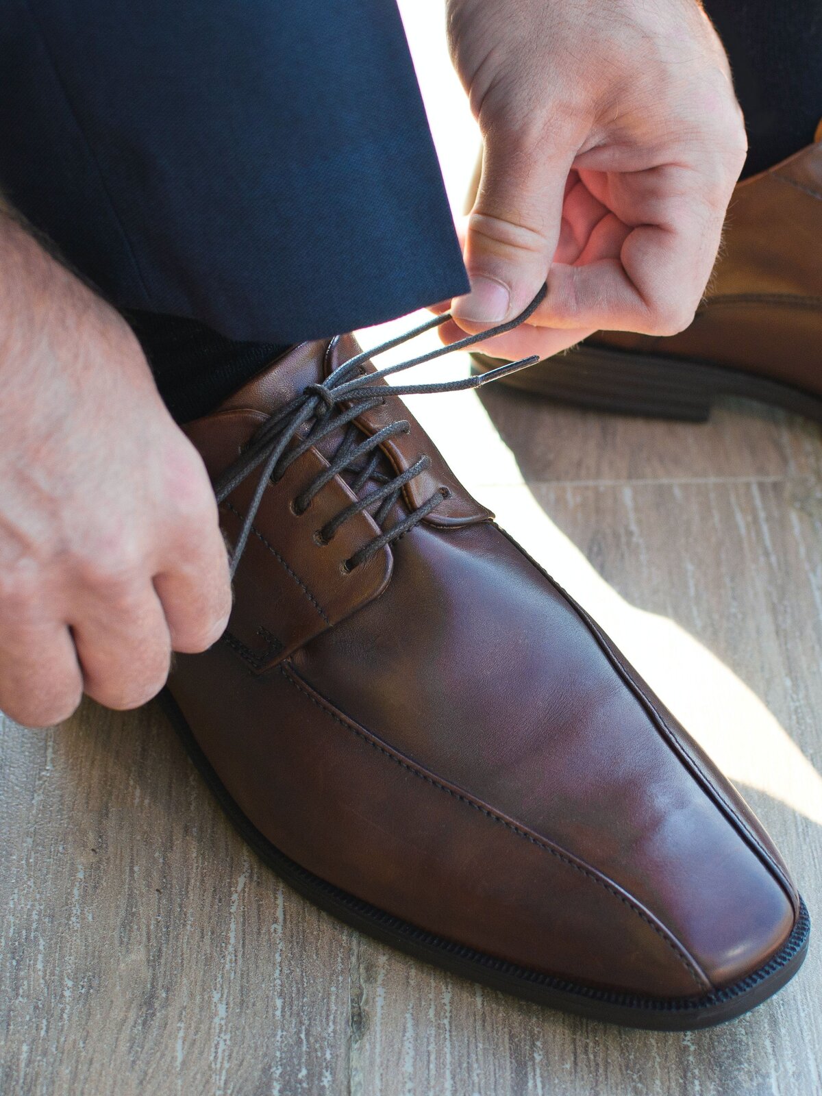 Zdjęcie przedstawia osobę wiążącą sznurowadło w eleganckich pantoflach z brąząwej skóry. 