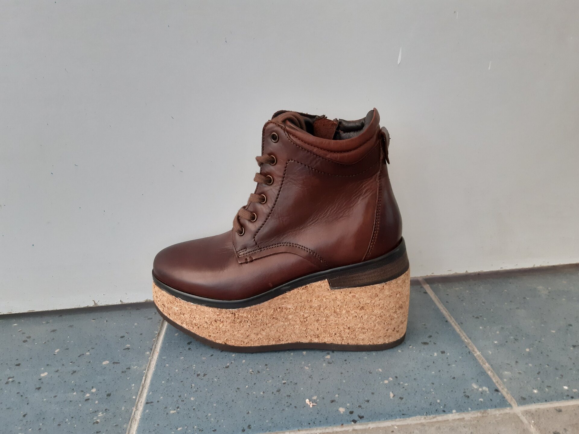 Zdjęcie przedstawia but z wysoką cholewką i sznurowaniem, który pod podeszwą ma swoje przedłużenie w formie korkowego koturnu.