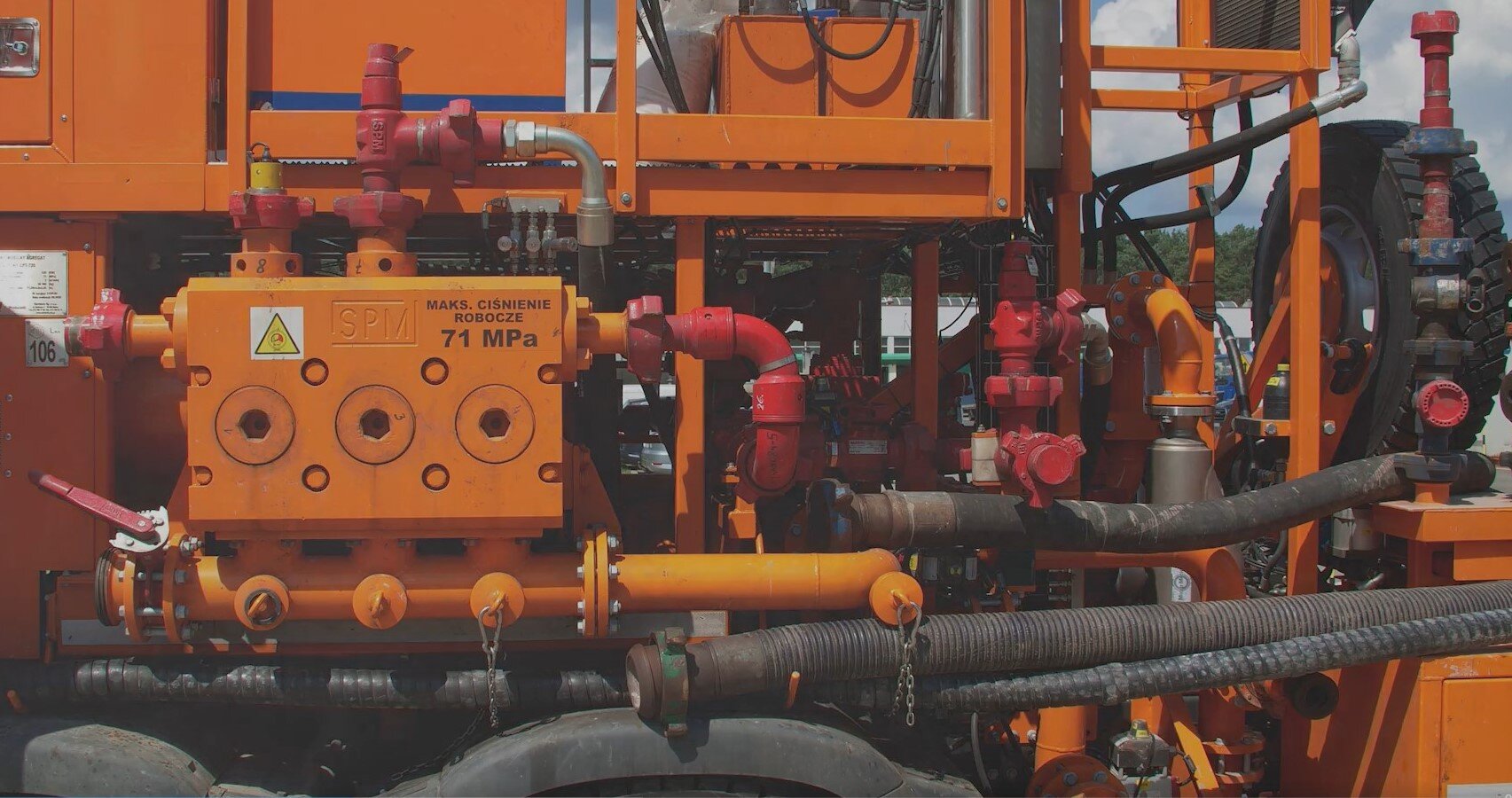 Na zdjęciu widać agregat cementacyjny na podwoziu samochodowym widzianym pod kątem od strony kabiny kierowcy.Agregat osadzony jest na podwoziu samochodowym, które ma cztery koła po każdej ze stron. Za kabiną kierowcy znajduje się duży pomarańczowy element o kształcie prostopadłościanu. Z przodu elementu są drzwi. Z tyłu podwozia samochodowego widać drabinę, rury oraz gumowe węże. Drabina jest przytwierdzona do boku samochodu.