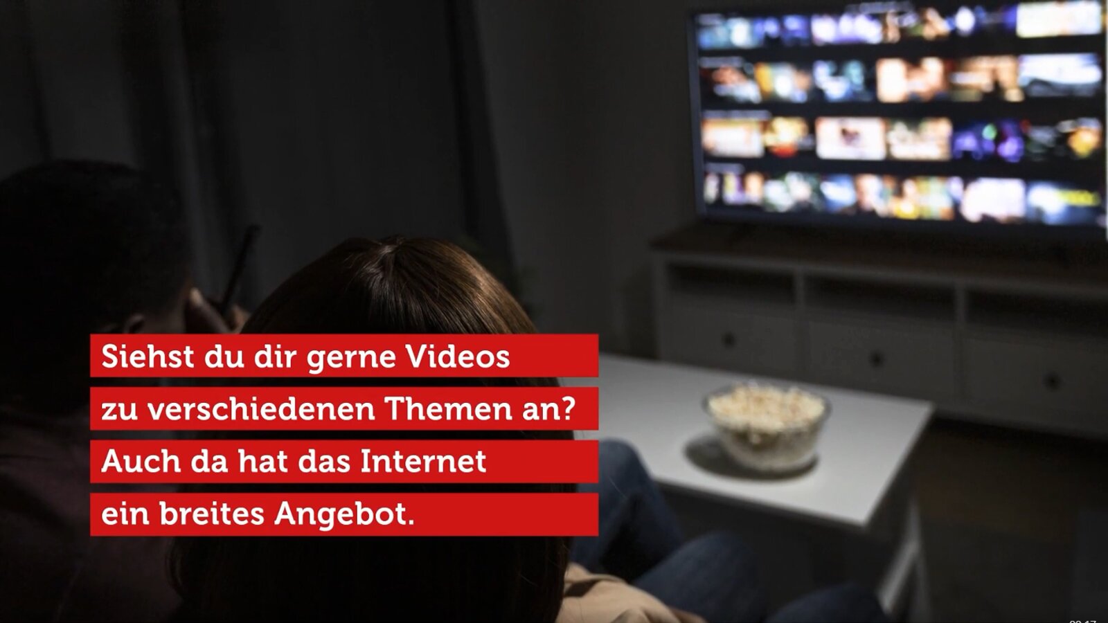 Ilustracja przedstawia wnętrze salonu i kobietę oraz mężczyznę siedzących przed ekranem telewizora. Na ilustracji wyświetla się napis: Siehst du dir gerne Videos zu verschiedenen Themen an? Auch da hat das Internet ein breites Angebot.