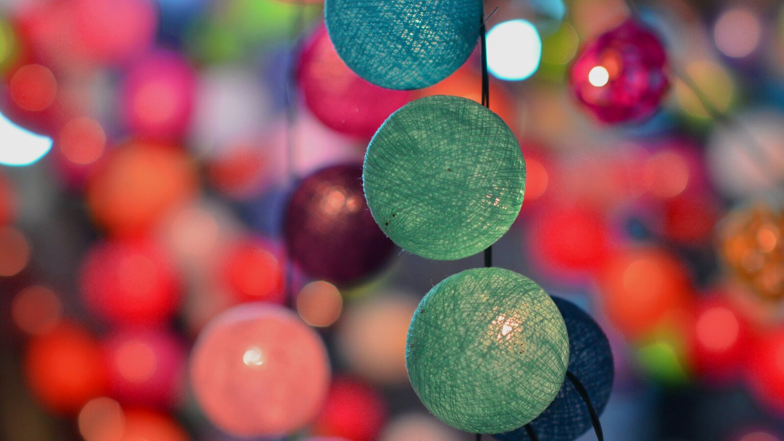 Na zdjęciu zostały przedstawione kolorowe świecące kule. Są wykonane z siatki bawełnianej, a w ich środku umiejscowione są lampki. Na pierwszym planie widać trzy świecące zielone kule połączone ze sobą kablem zasilającym. W tle widać kolorowe kule.