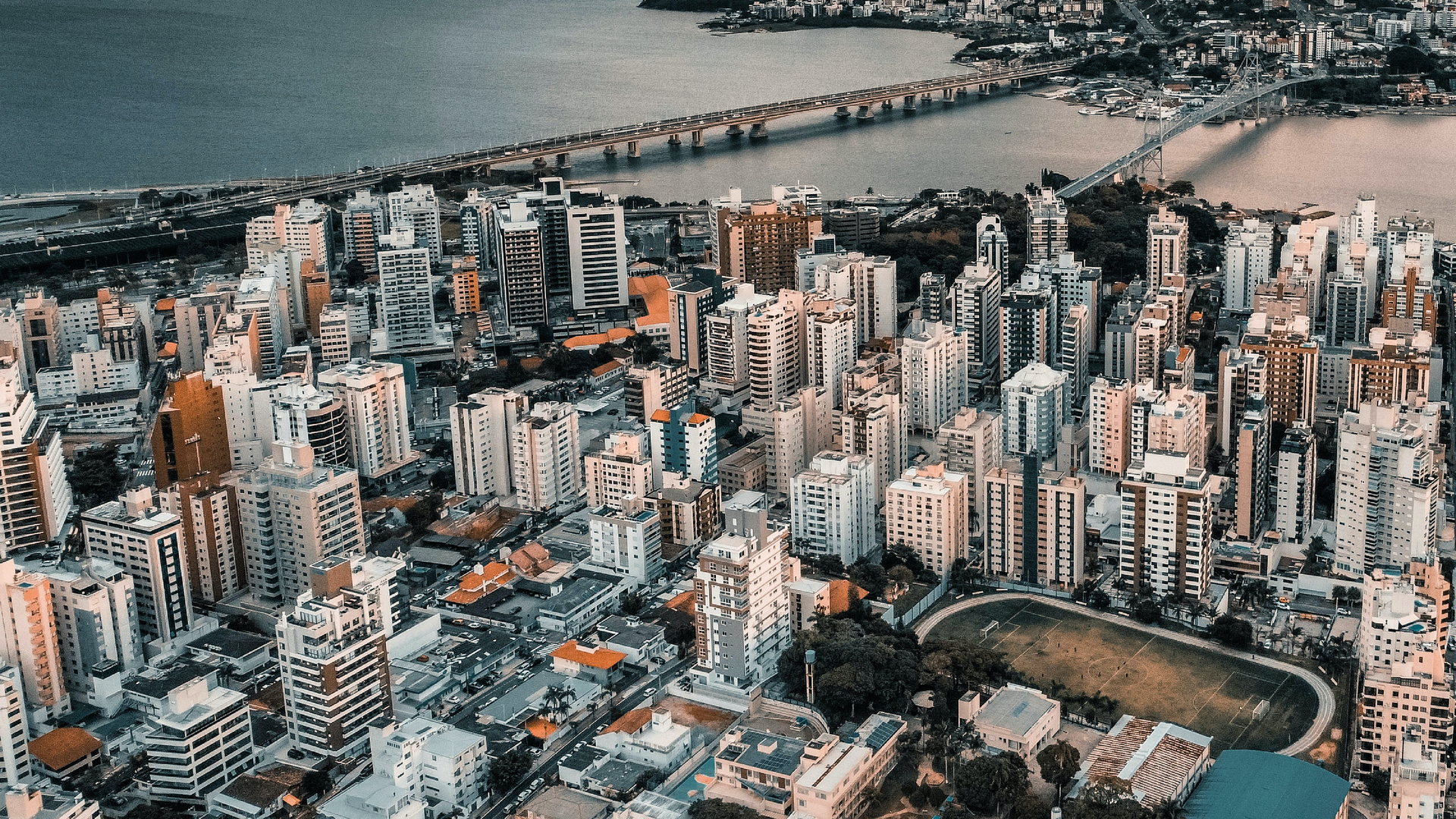 Zdjęcie przedstawia centrum dużego miasta z lotu ptaka. Widoczne są wysokie wieżowce. Miasto usytułowane jest nad morzem, widoczny są mosty.