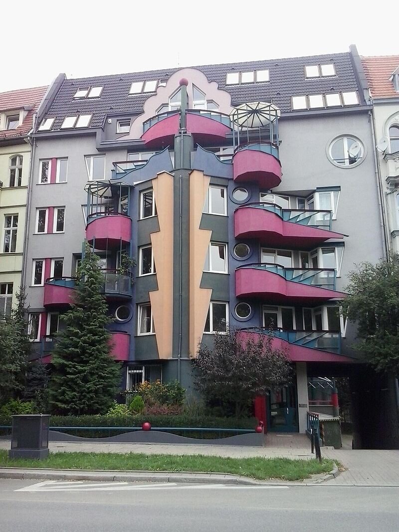 Zdjęcie przedstawia nowoczesny budynek mieszkalny wybudowany między dwoma innymi, starymi budynkami.