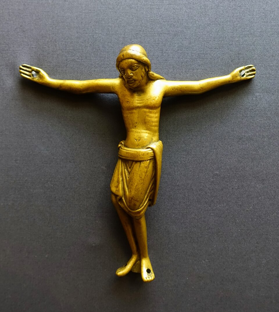 Romańska rzeźba Chrystusa Ukrzyżowanego z brązu: smukła postać o rozłożonych ramionach, z lekko pochyloną głową i skrzyżowanymi stopami, ubrana w krótkie perizonium; figura na jednolitym, ciemnym tle.