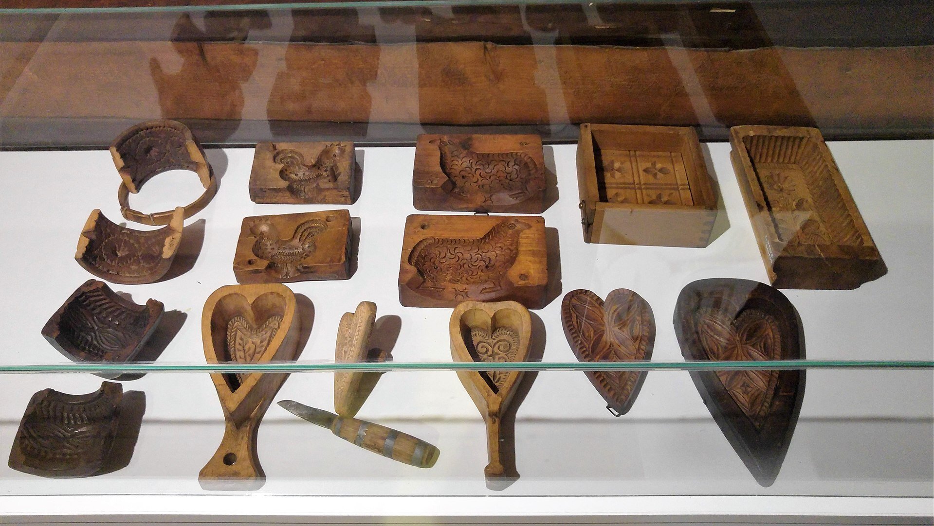 Zdjęcie przedstawiające ułożone w gablocie drewniane formy w kształcie serc, prostokątów, lub zwierząt. Posiadają wyryte ozdobne kształty.