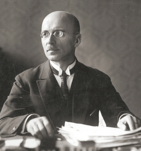 Czarno‑białe zdjęcie przedstawia Jana Stanisława Jankowskiego. Jest to mężczyzna łysy, w sile wieku. Jego głowa zwrócona jest w prawą stronę. Na nosie ma małe okulary. Ubrany jest w ciemny garnitur, białą koszulę i ciemny krawat. Mężczyzna siedzi przy stole. Lewą rękę trzyma opartą na pliku kartek.