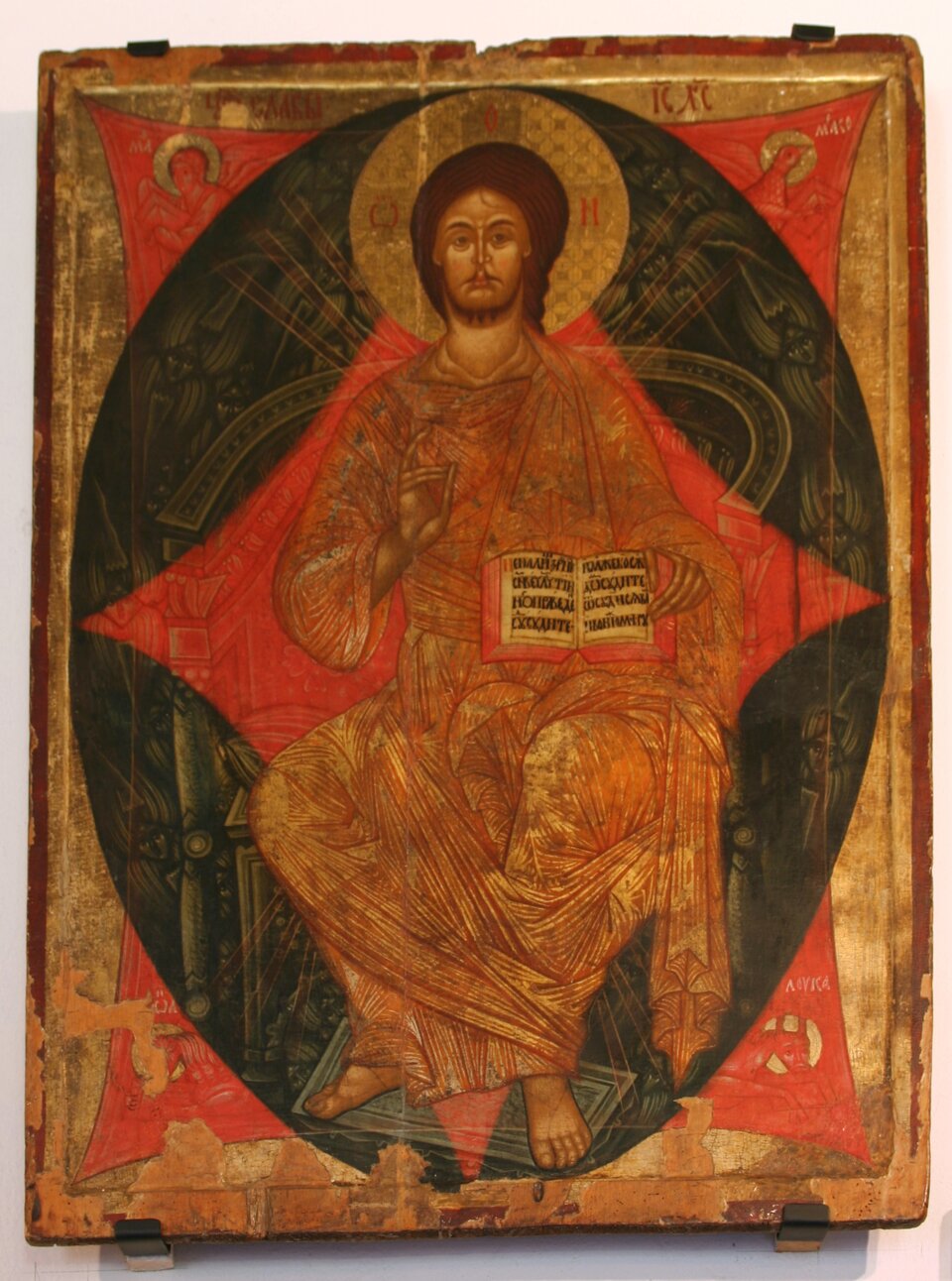 Ikona Chrystusa Pantokratora siedzącego frontalnie na tronie, ujętego w migdałowatą mandorlę w kolorach czerni i czerwieni. Chrystus ma długie włosy, brodę i złoty nimb z krzyżem wokół głowy. Prawą ręką wykonuje gest błogosławieństwa, a w lewej trzyma otwartą księgę z tekstem w języku cerkiewnosłowiańskim. Ubrany jest w złocisto‑czerwone szaty o gęstym, linearnym układzie fałd. Tło ikony jest złote, z widocznymi przetarciami i ubytkami farby, co podkreśla jej wiek i sakralny charakter.