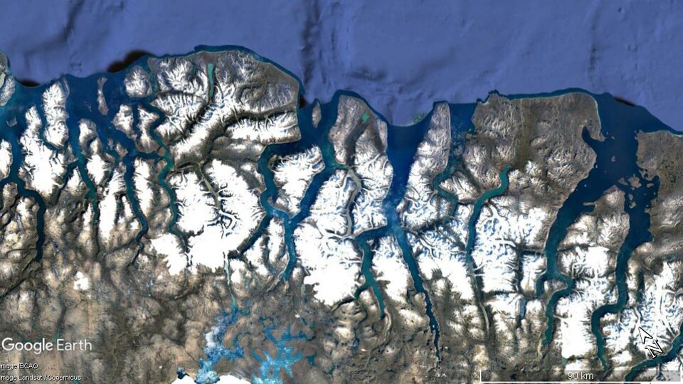 Zdjęcie satelitarne przedstawia wybrzeże fiordowe. Ląd zaznaczony jest kolorem białym i szarym, a woda turkusowym. Na brzegu tworzą się długie i rozgałęzione zatoki prowadzące w głąb lądu.