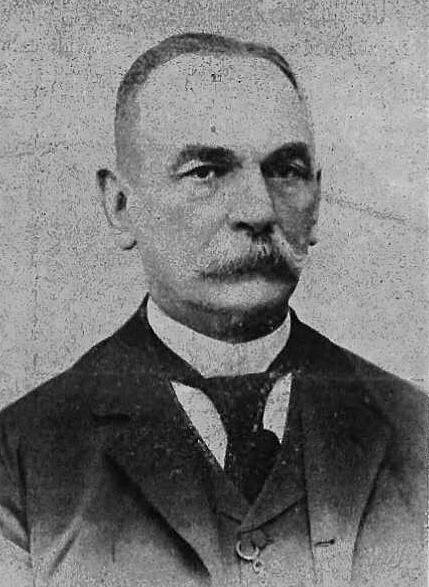 Portret dojrzałego mężczyzny. Postać ukazana jest od piersi w górę. Mężczyzna prezentuje prawy półprofil. Jego twarz jest owalna. Mężczyzna ma wysokie, gładkie czoło. Włosy mężczyzny są bardzo krótkie, gładko zaczesane do tyłu. Postać ma duże, lekko odstające uszy. Postać ma ciemne i grube brwi. Jego oczy są zwężone, patrzą w dal. Nos mężczyzny jest duży, szeroki, prosty. Mężczyzna ma gęste wąsy zasłaniające wargi. Jest ubrany w koszulę, kamizelkę i surdut. Na szyi ma zawiązany krawat. Do górnej dziurki do guzika kamizelki ma przyczepiony łańcuszek do zegarka.