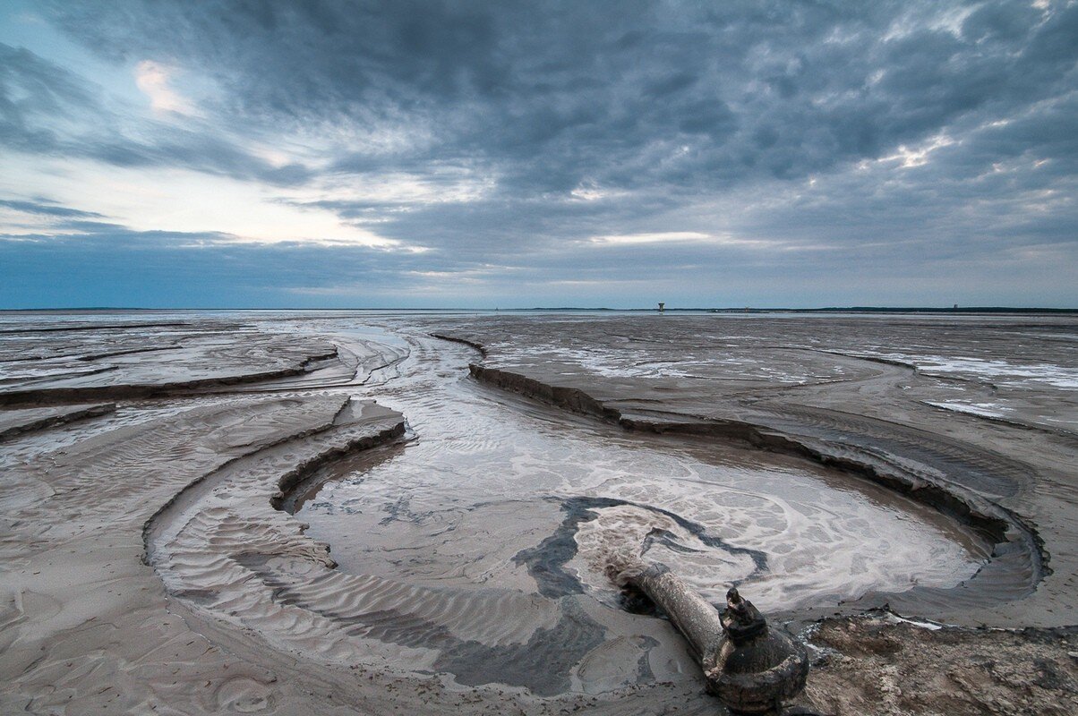 Zdjęcie przedstawia Żelazny Most. Jest to półokrągłe zagłębienie w ziemi wypełnione odpadami poflotacyjnymi o szarym zabarwieniu. Na brzegach znajduje się piasek.