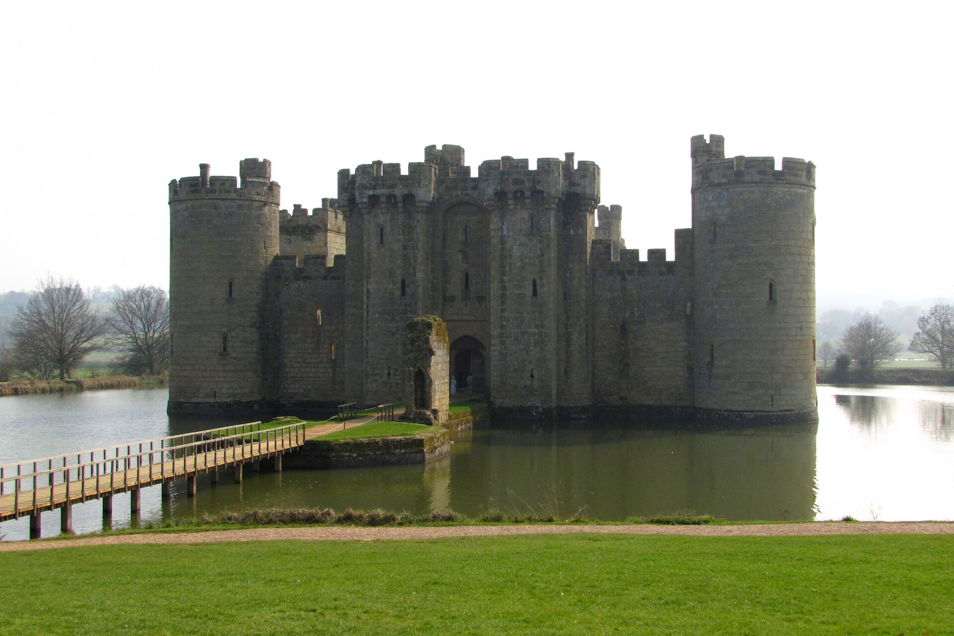 Zdjęcie przedstawia zamek. Zamek posiada grube i wysokie mury i wieże. Stoi na wyspie otoczonej wodą. Do zamku prowadzi most zawieszony nad wodą.