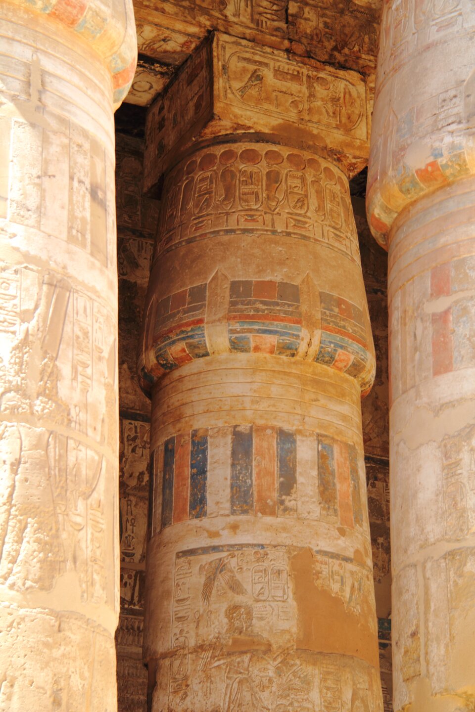 Fotografia ukazuje masywne kolumny egipskie w części wewnętrznej świątyni Chonsu, wykonane z piaskowca i częściowo zachowane w oryginalnej polichromii. Kadr ukazuje trzon zdobiony kolorowymi pasami. Na trzonie kolumny znajdują się reliefy. Kapitel kolumny ma formę zamkniętego kwiatu lotosu. Nad kapitelem widoczny jest fragment belkowania z barwionymi reliefami. 