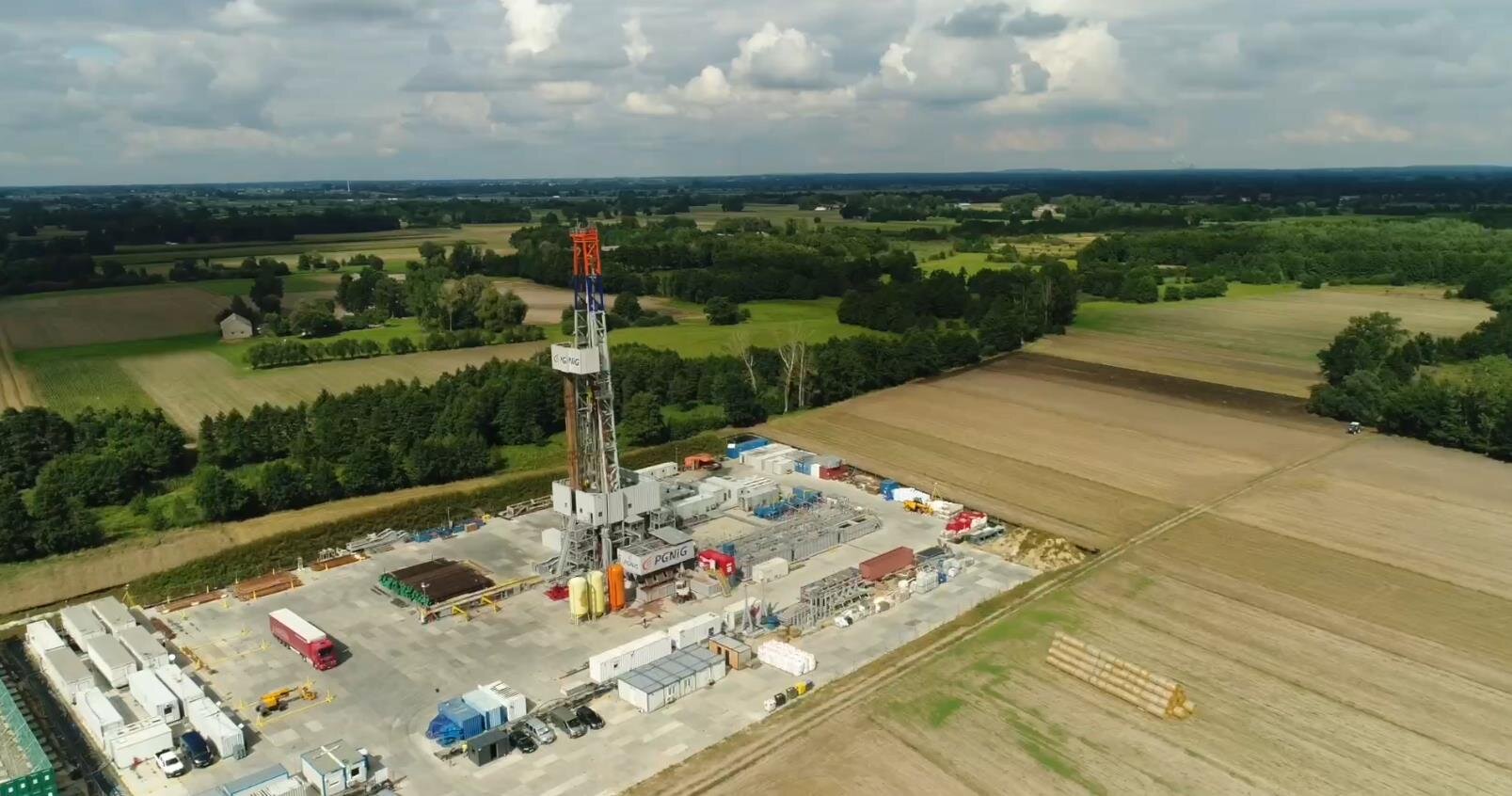 Na zdjęciu widoczny jest wieżomaszt wraz z placem widoczny z lotu ptakaPlac wiertniczy widoczny jest pod kątem lotu ptaka. Plac ma kształt prostokąta. Podstawa placu jest wyłożona betonowymi płytami. W centralnym punkcie placu znajduje się wieżomaszt. Wieżomaszt jest w kształcie litery A. Wieżomaszt ma dwa galerie. Na dolnej większej galerii znajduje się podbudówka. Podbudówka wykonana jest z blachy falistej. Na górnej podbudówce widać napis: PGNiG.Wieżomasz znajduje się pomiędzy małymi obiektami przypominającymi kontenery. W tle zdjęcia widać tereny leśne.