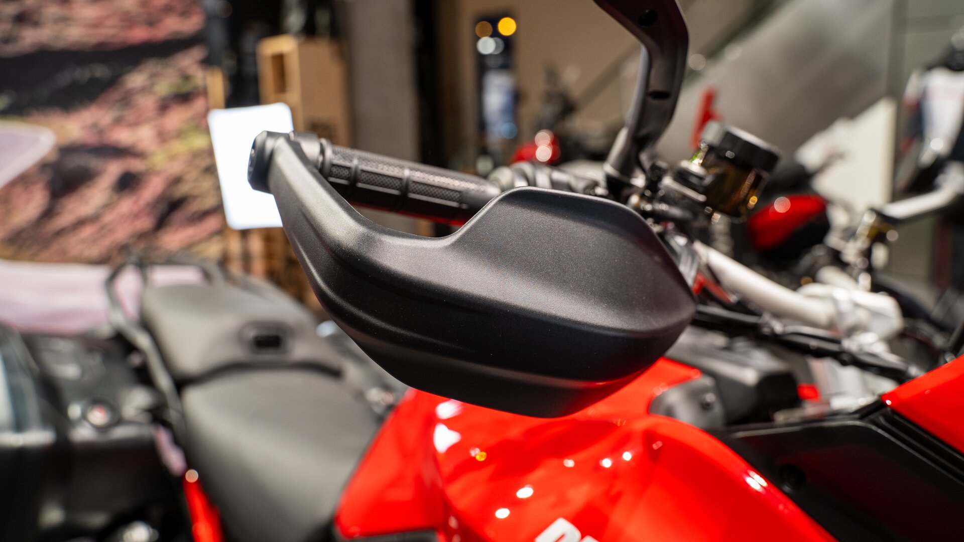 Zdjęcie przedstawia kierownicę motocykla. Do uchwytu kierownicy przymocowana jest osłona chroniąca dłoń.  