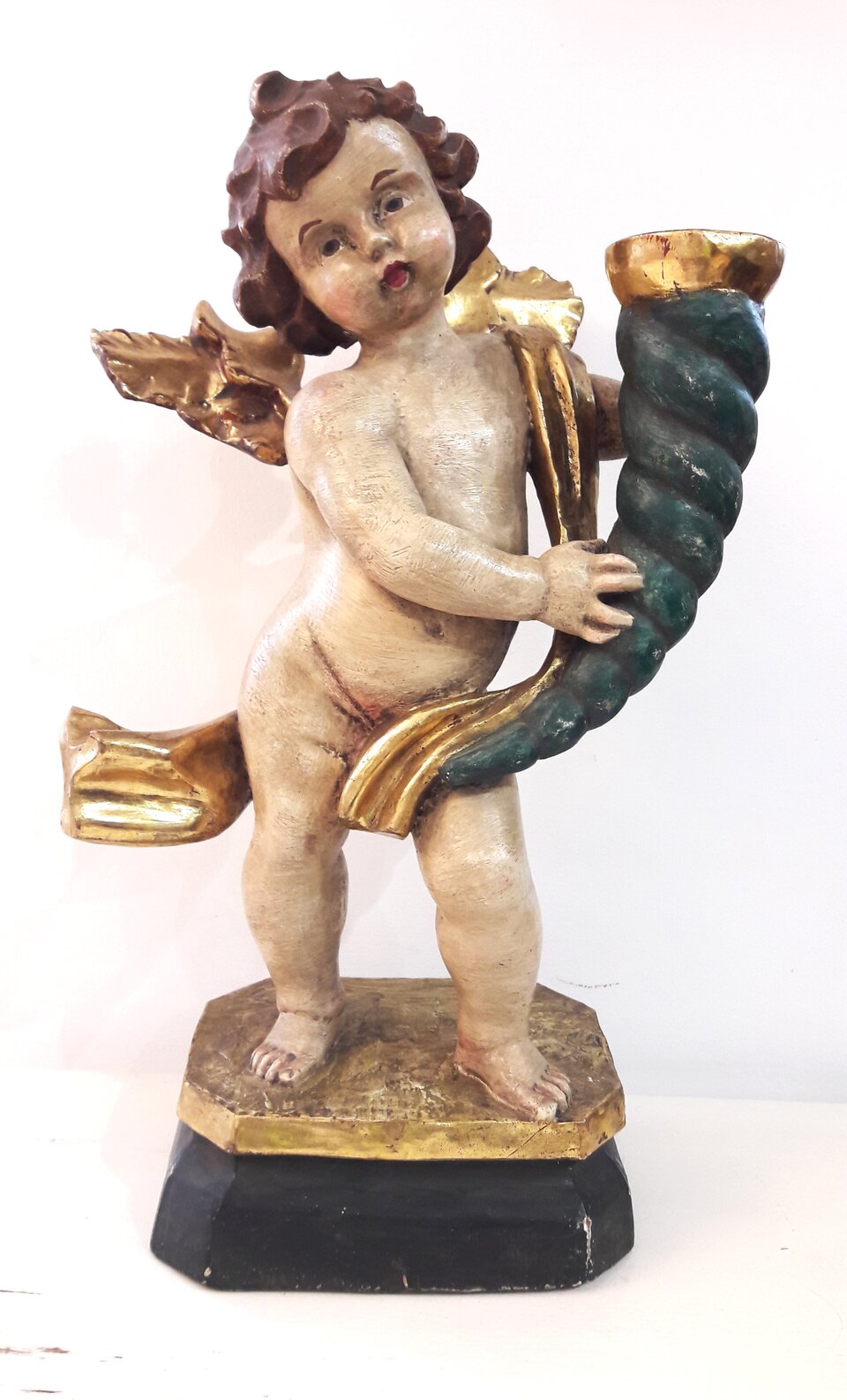 Ilustracja przedstawia rzeźbę zatytułowaną „Putto z rogiem obfitości”. Ukazuje nagiego, małego, pulchnego amorka ze złoconymi skrzydełkami, trzymającego ciemnoniebieski róg. Przez ramię chłopca przełożona jest złocona szarfa.