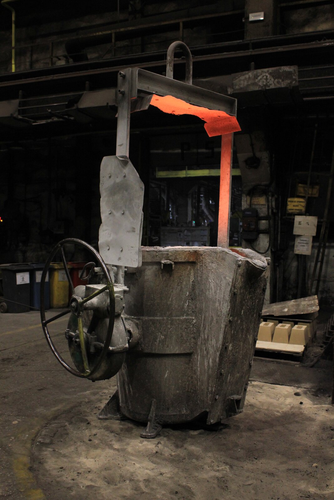 Na ilustracji widoczna jest kadź odlewnicza. Jest to duży obiekt w kolorze szarym, przypominający pojemnik. Stoi ona na podłożu, zwrócona szyjką w prawą stronę. Kadź posiada uchwyt w kształcie ramienia, doczepionego do jej boków. Jest on oświetlony od spodu rozgrzanym stopem, który znajduje się wewnątrz kadzi.