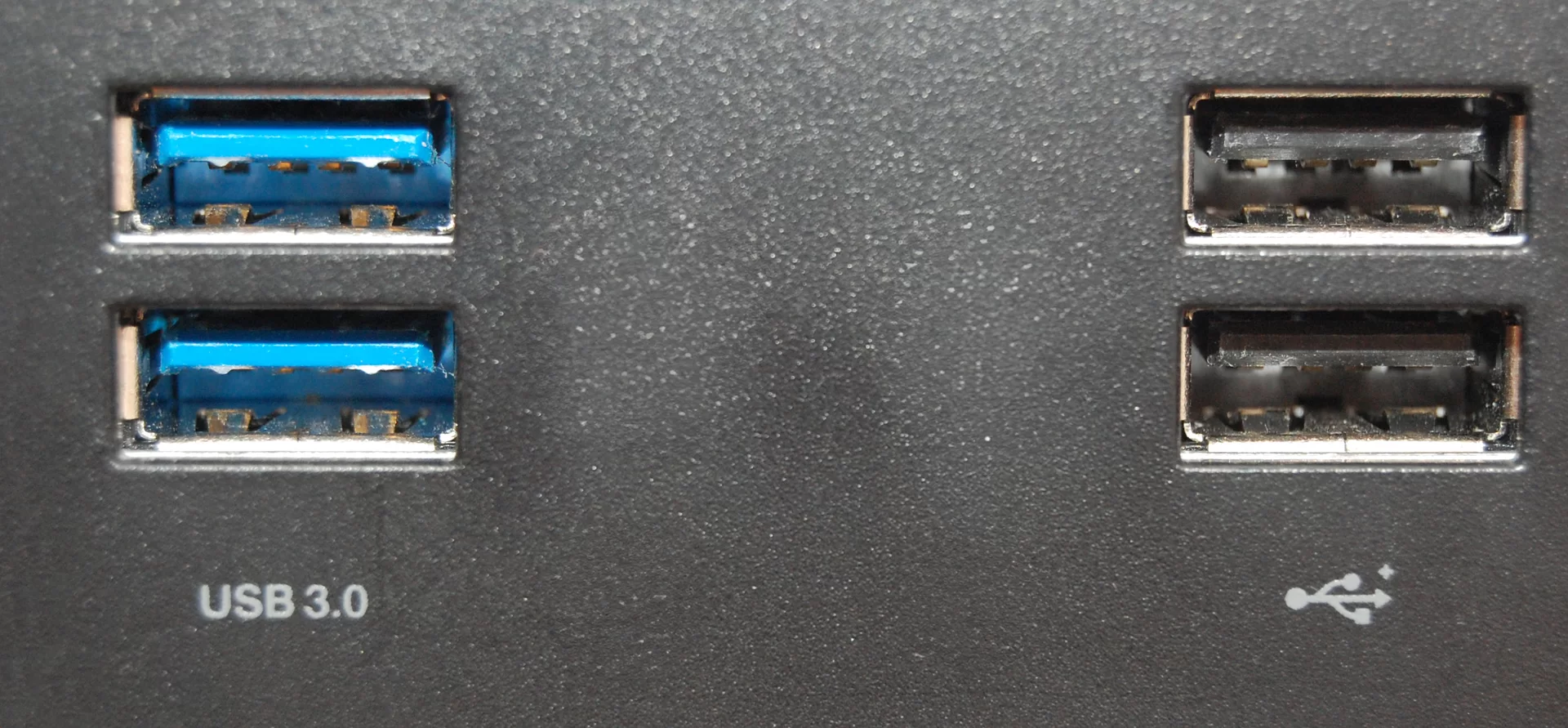 Fotografia przedstawiająca cztery gniazda USB. Po lewej znajdują się dwa prostokątne niebieskie otwory z odstającą w środku płaską płytką/stykiem. Podpisane są USB 3.0. Po prawej znajdują się dwa prostokątne czarne otwory z odstającą w środku płaską płytką/stykiem. Są to gniazda USB 2.0, pod nimi znajduje się główne logo standardu USB.