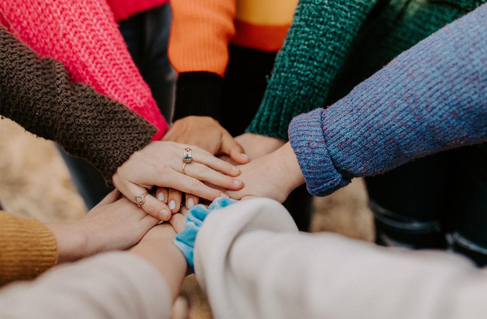 Zdjęcie przedstawia ręce ośmiu osób stojących w kręgu, a ich dłonie są położone pośrodku jedna na drugiej.