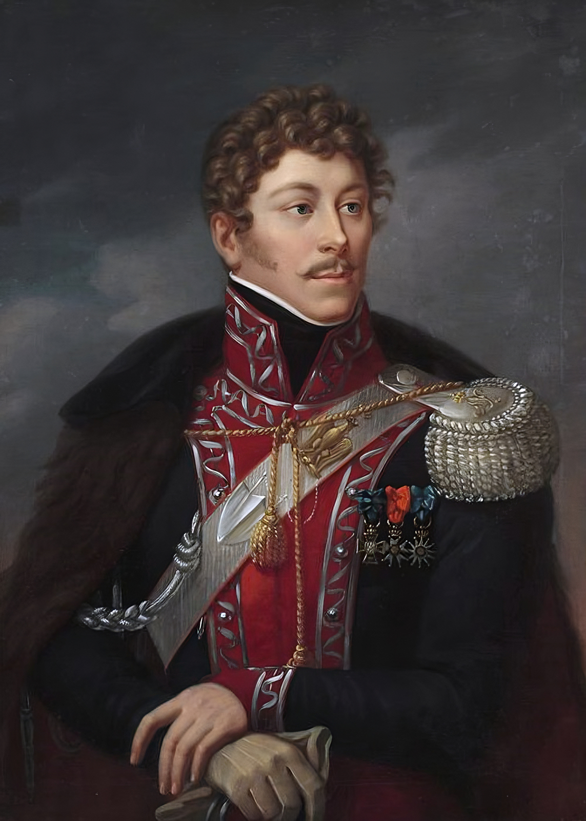 Zdjęcie przedstawia portret Jana Hipolita Kozietulskiego w mundurze z czasów napoleońskich. Mężczyzna o zakręconym wąsie, kręconych włosach zwrócony jest twarzą ku prawej krawędzi obrazu. Ciemny, wysoki kołnierz jest zasłonięty przez kołnierz munduru oficerskiego z trójkątnym wcięciem w dół. Na piersi widoczny jest złoty pas z frędzelkami i splotem na wysokości klatki piersiowej, spinający płaszcz. Lewe ramię wystaje wyraźnie spod płaszcza, odsłaniając pagon i dystynkcje oficerskie na ramieniu. Na lewej piersi oficer nosi trzy ordery, wśród nich jeden to Virtuti Militari, znajdujący się w pośrodku. Ręce splatają się dłońmi, lewa chwyta od góry nadgarstek prawej. Mundur zdobiony srebrnymi motywami geometrycznymi i guzkami. Namalowane tło prezentuje fragment zachmurzonego nieba.