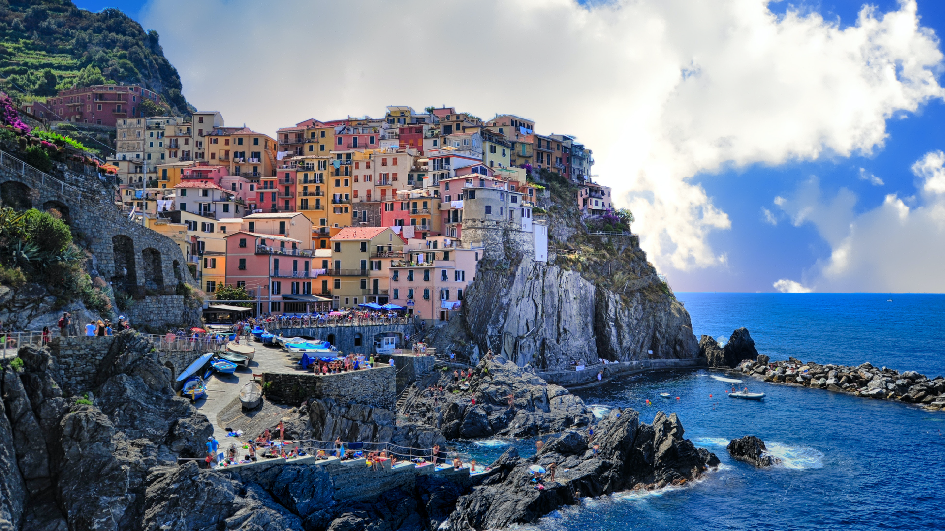 Zdjęcie przedstawia malownicze miasteczko na wybrzeżu liguryjskim. Widoczne są domy usytułowane kaskadowo na skale. Widoczna jest zatoka, w której znajduje się miasteczko. Nie ma tutaj plaży, wybrzeże jest skaliste.