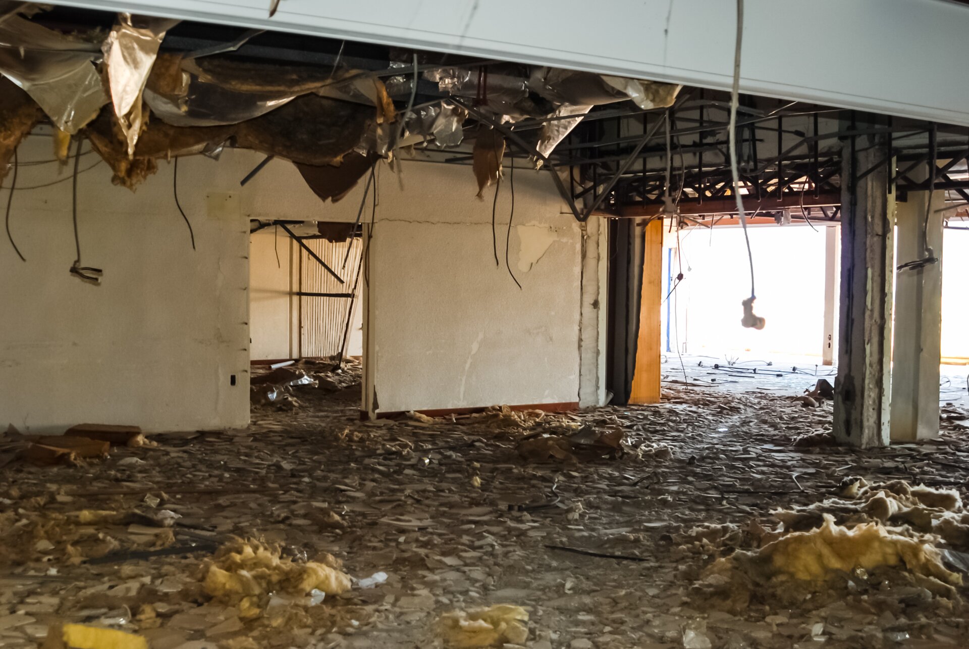 Zdjęcie przedstawia uszkodzenia izolacji termicznej stropów. Widoczne jest rozległe uszkodzenie. Resztki izolacji leżą na podłodze lub zwisają ze stropu.
