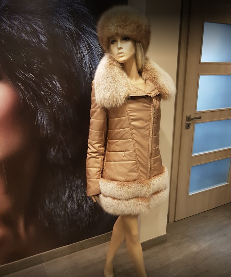 Na zdjęciu widoczna kurtka w beżowym kolorze sięgająca do połowy uda. Materiał jest błyszczący, dół kurtki i kołnierz są obszyte jasnym, kremowym futrem. Nagranie tożsame z treścią.