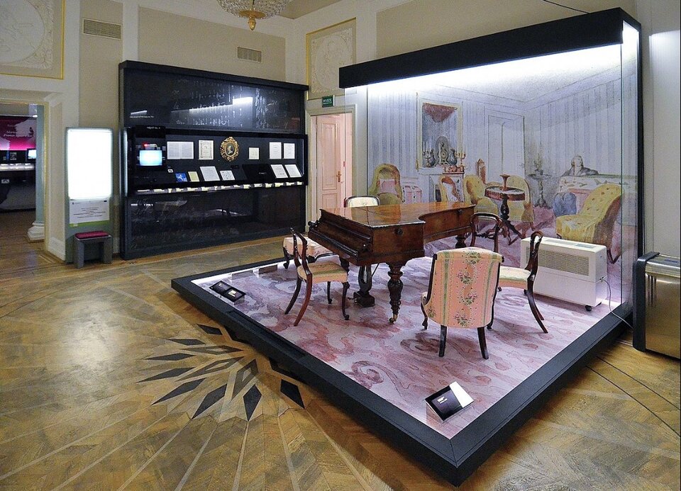 Fotografia przedstawia wnętrze Muzeum Fryderyka Chopina w Warszawie, gdzie jest wystawiony ostatni fortepian Chopina. Fortepian jest na podium, w otoczeniu wyposażenia sali muzealnej.