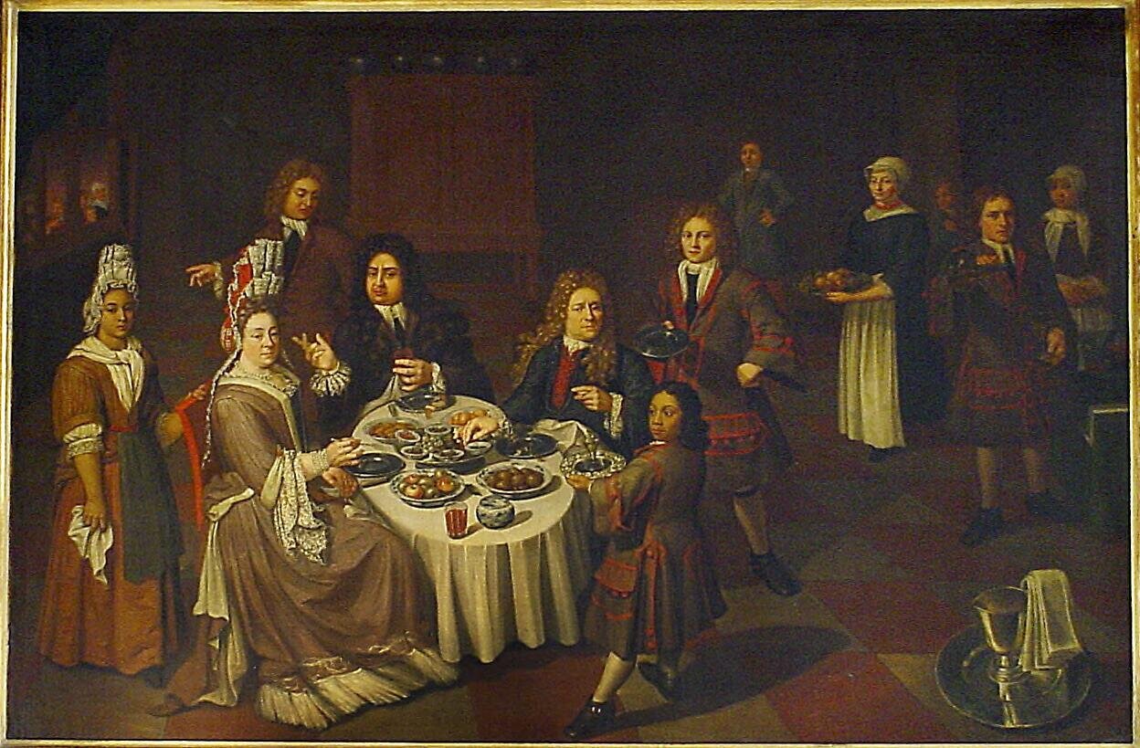 Ilustracja przedstawia troje ludzi, dwóch mężczyzn i kobietę, siedzących przy okrągłym stole i spożywających posiłek. Kobieta ubrana jest w długa suknię wykończoną koronkowymi obszyciami. Na głowie na wysoki czepiec także zdobiony koronką. Obaj mężczyźni mają na głowach peruki z kręconymi, długimi włosami sięgającymi połowy pleców, ubrani są w marynarki, kamizele i koszule. Wokół nich kręcą się służący i służące donoszący jedzenie i picie.