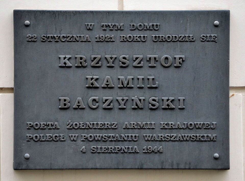 Fotografia przedstawia tablicę pamiątkową wiszącą na ścianie budynku. Umieszczono na niej napis: W tym domu 22 stycznia 1921 roku urodził się Krzysztof Kamil Baczyński, poeta, żołnierz Armii Krajowej. Poległ w Powstaniu Warszawskim 4 sierpnia 1944.