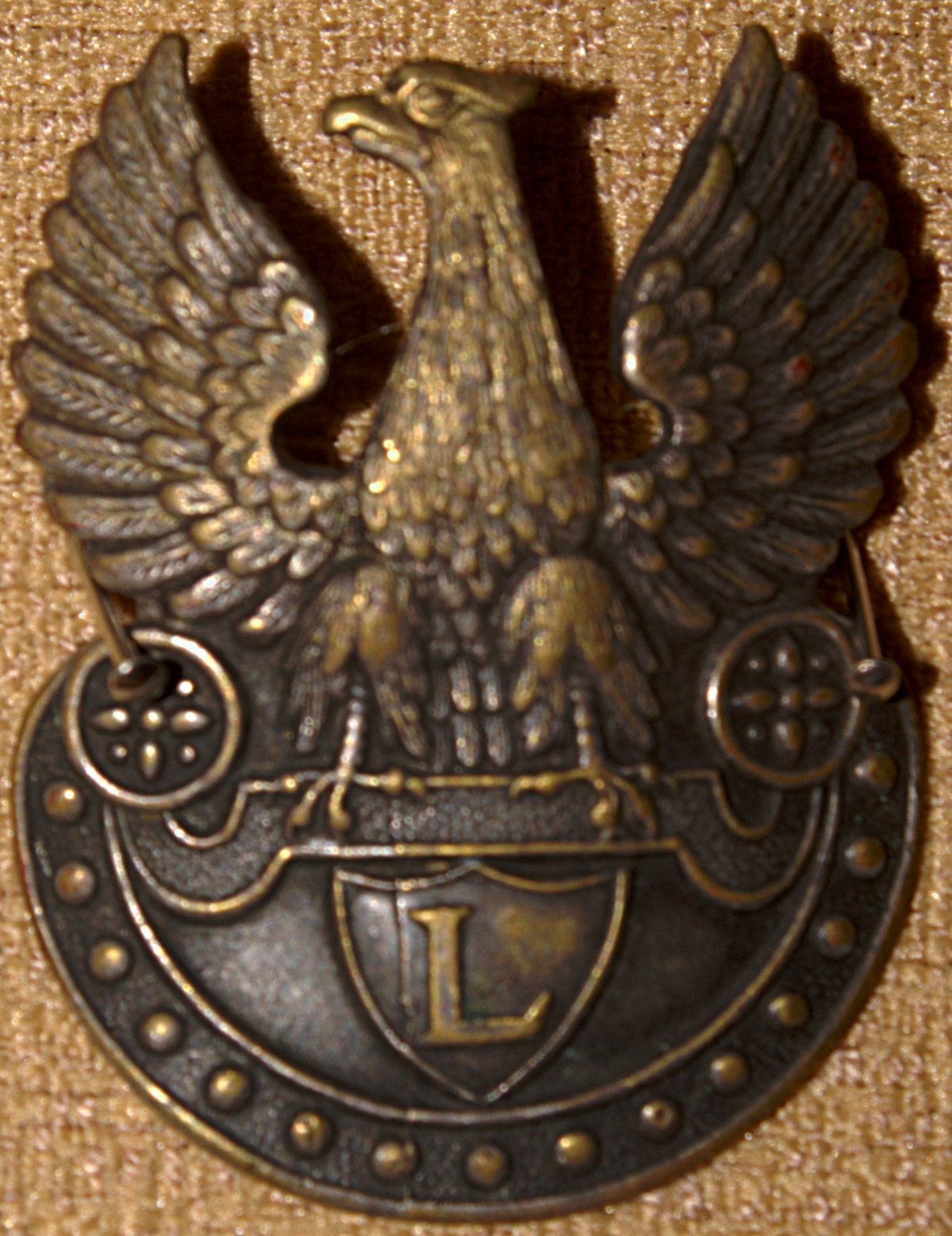 Zdjęcie przedstawia stalowego orła legionowego z wzniesionymi do wysokości głowy skrzydłami, orzełek trzyma w szponach tarczę z literą L. 
