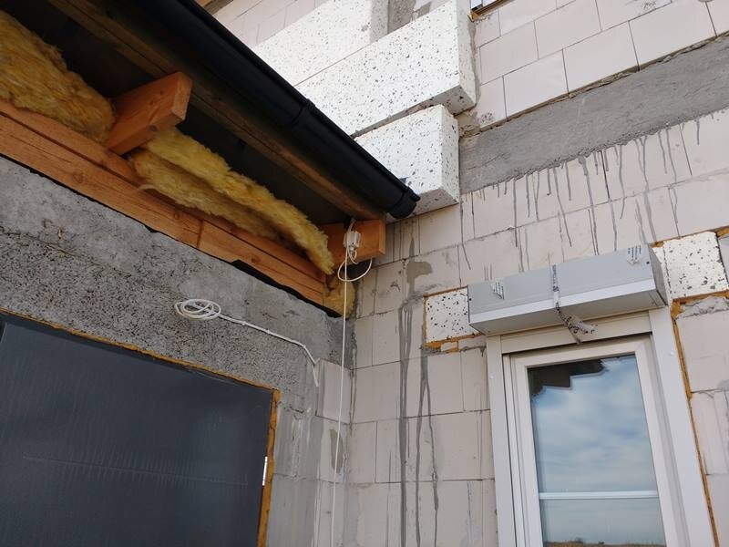 Na zdjęciu ukazano czujnik temperatury zewnętrznej umieszczony pod okapem dachu na zewnątrz budynku będącego w budowie.
