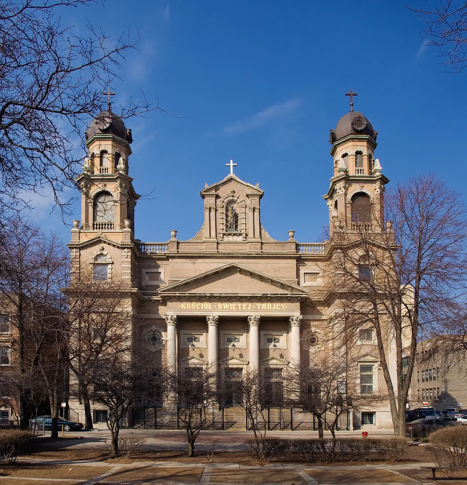 Zdjęcie kościoła, który ma dwie wieże. Na górze każdej wieży jest krzyż. Po środku jest wejście do kościoła, które zdobią cztery kolumny. Na górze budynku jest wizerunek świętego.  