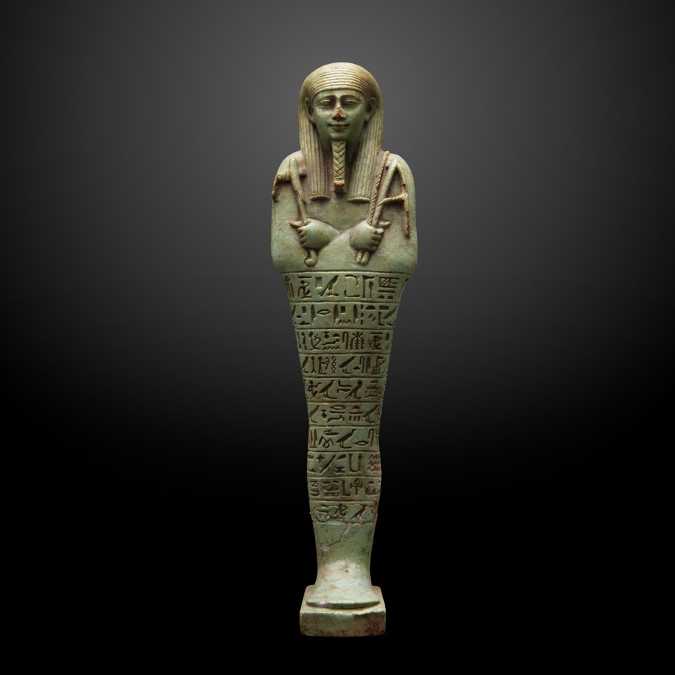 Zdjęcie przedstawia uszebti faraona Neferitesa I, władcy XXIX dynastii . Postać ukazana jest frontalnie z nogami złączonymi, w sztywnej, wertykalnej pozie, imitującej zwój mumii. Ręce skrzyżowane są na piersi i trzymają atrybuty – dwie motyki (symbol pracy rolniczej w zaświatach). Fryzura kobiety symetrycznie opada na ramiona. Twarz jest realistyczna, z podkreślonymi oczami, brwiami i uśmiechniętymi ustami. Uwagę zwraca drobiazgowe opracowanie detali, zwłaszcza brody ceremonialnej – świadczącej o wysokim statusie przedstawionej osoby.  Na powierzchni korpusu widnieje inskrypcja zapisana w postaci hieroglifów. 